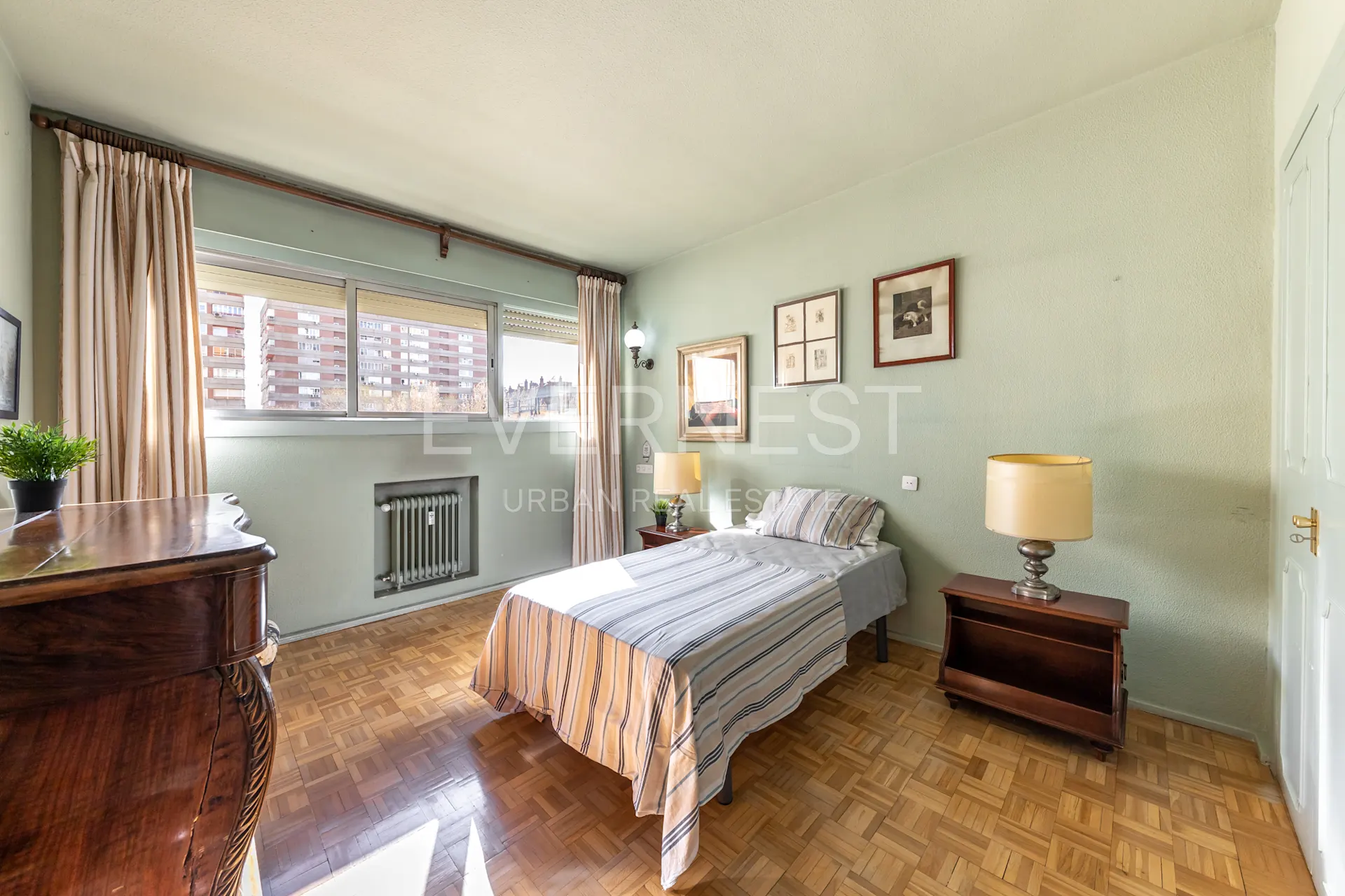 Helles Schlafzimmer mit Einzelbett, großem Fenster, Nachttischen und Bildern an der Wand.