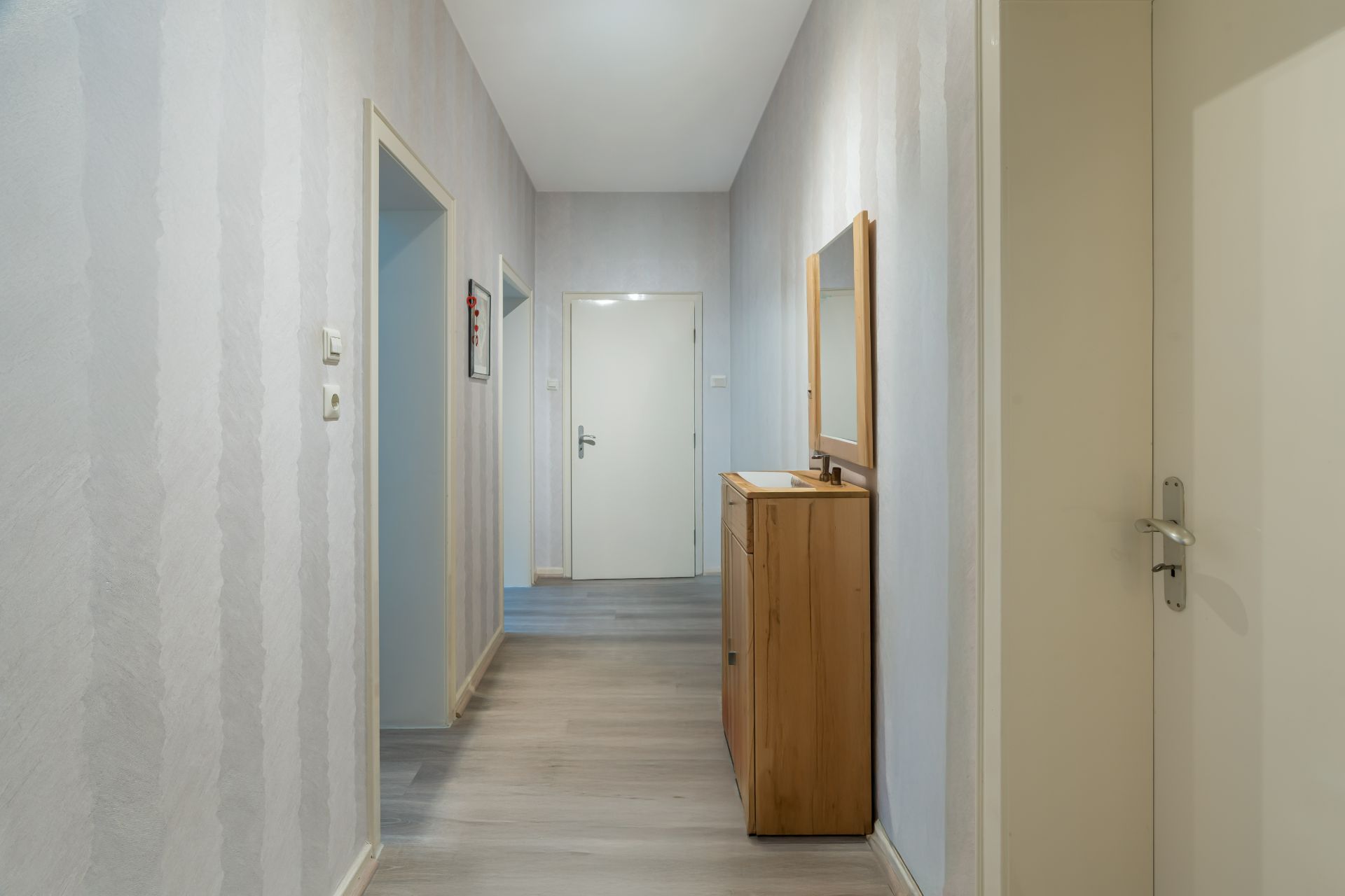 Heller Flur mit Holzmöbel und Spiegel, mehreren Türen und grauen Wänden.