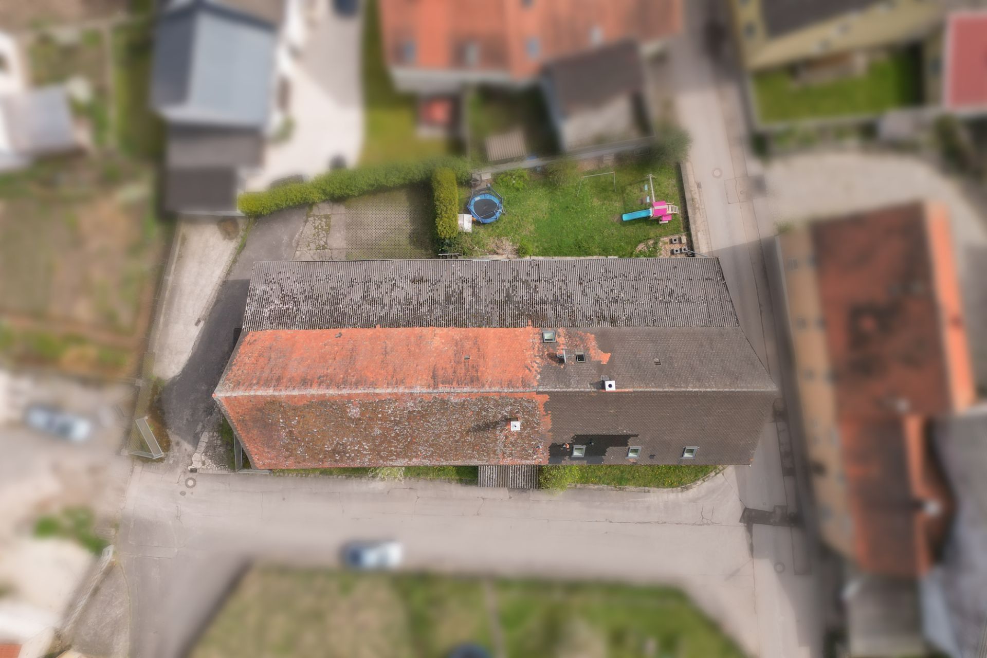 Luftaufnahme eines langgestreckten Wohnhauses mit Garten und Kinderspielgeräten.