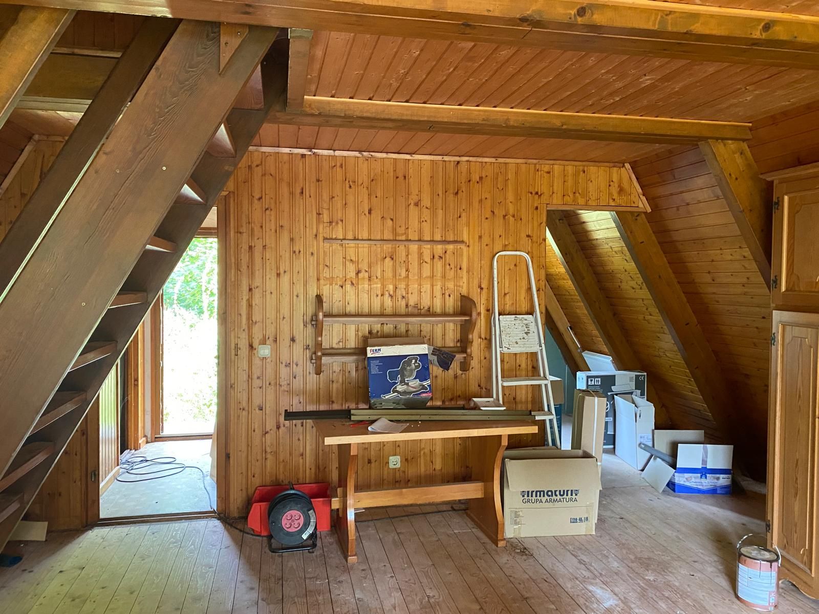 Holzwandzimmer mit Treppe, Tisch, Leiter und mehreren Kartons.