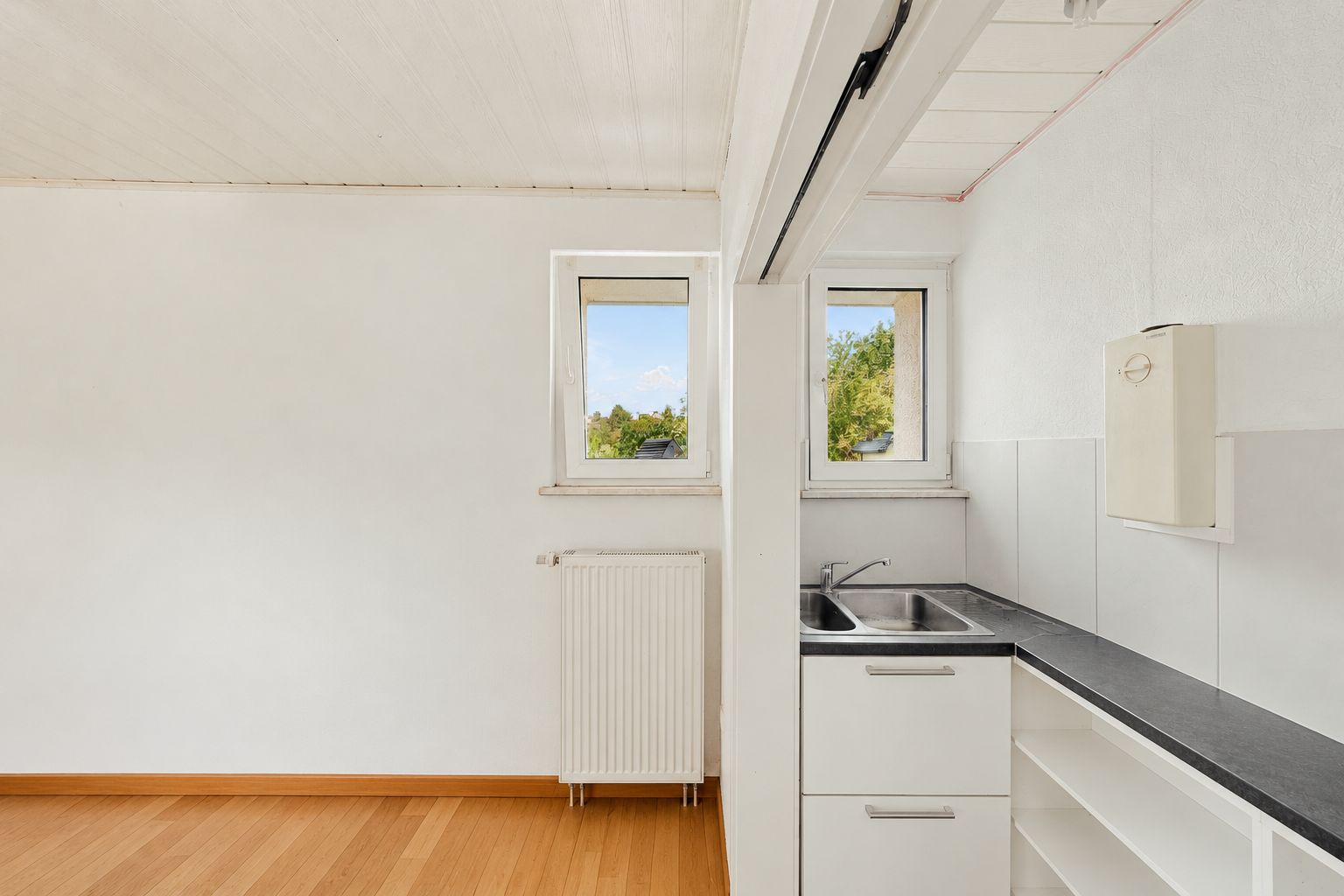 Helle Küche mit Spüle, weißem Schrank, zwei Fenstern und Heizkörper auf Holzfußboden.