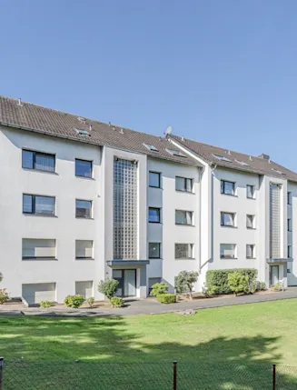 Mehrfamilienhaus mit vier Stockwerken, Glasbausteinen im Treppenhaus und großem Grünbereich davor.
