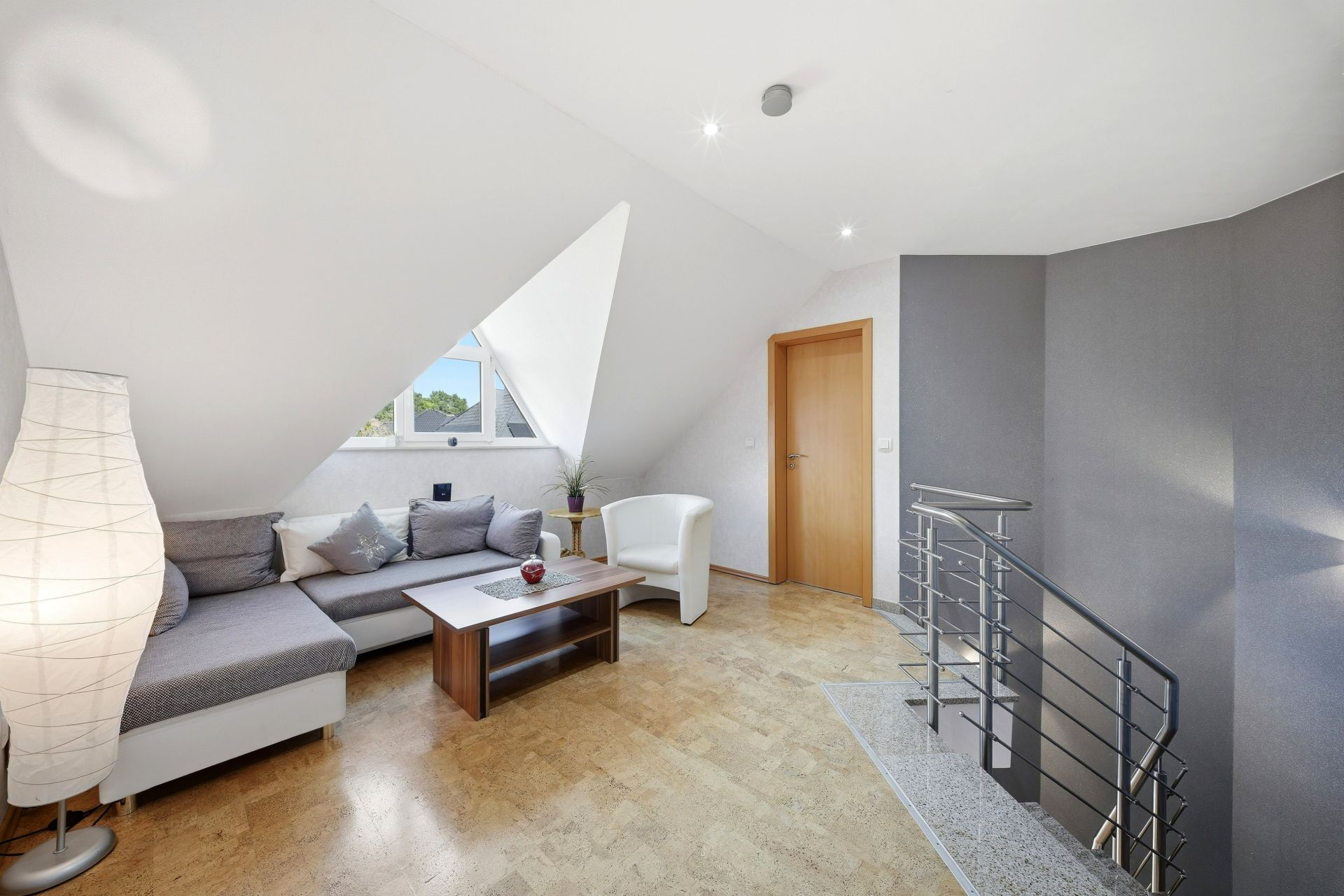 Modernes Wohnzimmer mit Ecksofa, Couchtisch, Sessel und Treppe, Fenster in Dachschräge.