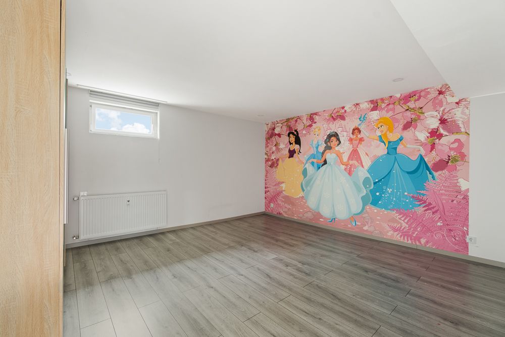 Leeres Zimmer mit Holzfußboden und bunter Märchenprinzessinnen-Tapete an der Wand.