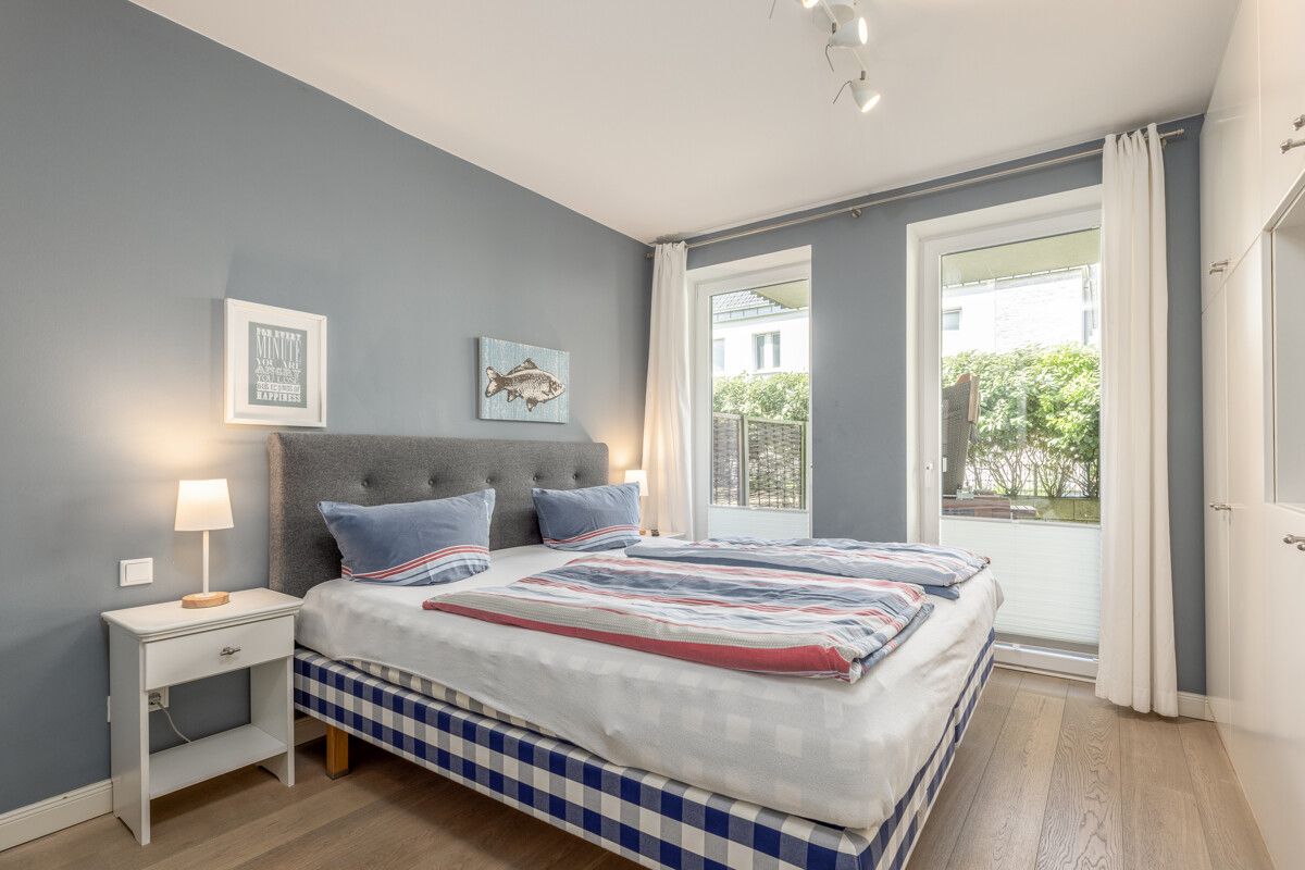 Helles Schlafzimmer mit Doppelbett, Nachttisch, Fenstern und blauer Wand.