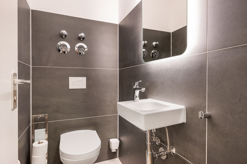 Modernes kleines Bad mit Wandtoilette, Waschbecken und beleuchtetem Spiegel.