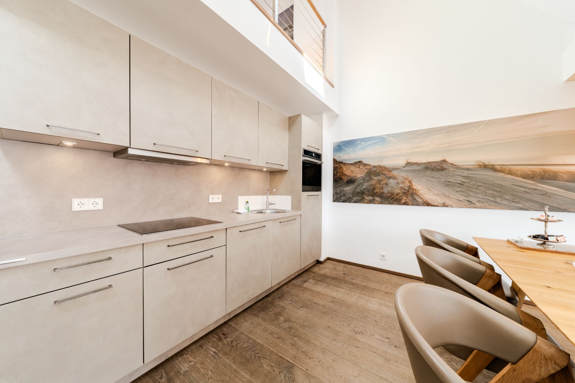Moderne, helle Einbauküche mit Holzboden und Essbereich, an der Wand ein großes Landschaftsbild.