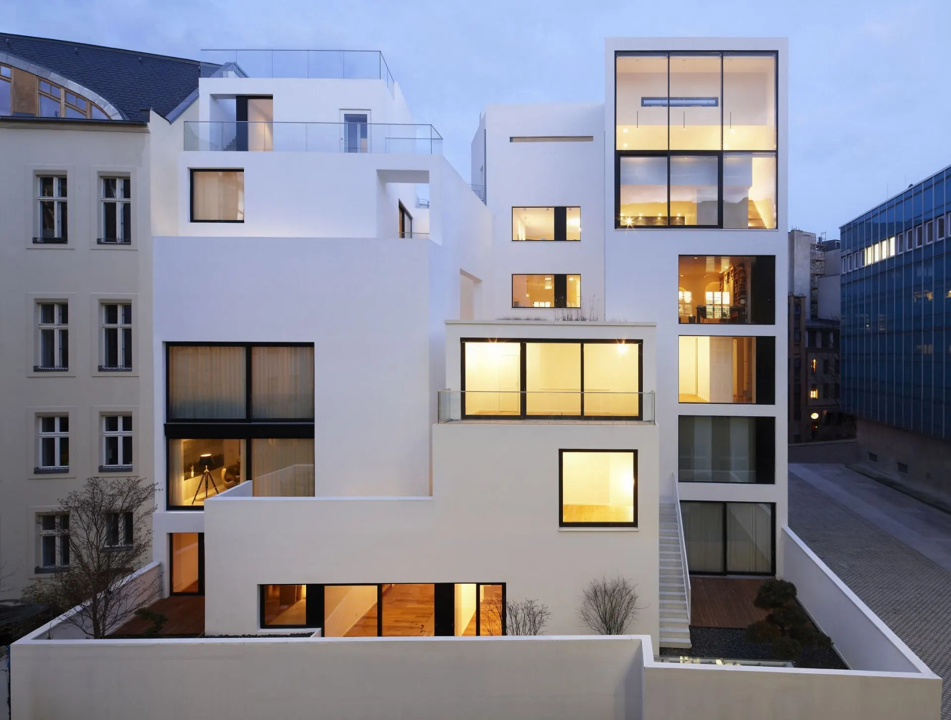 Moderne, mehrstöckige Wohngebäude mit großen Fenstern und weißen Fassaden bei Dämmerung.