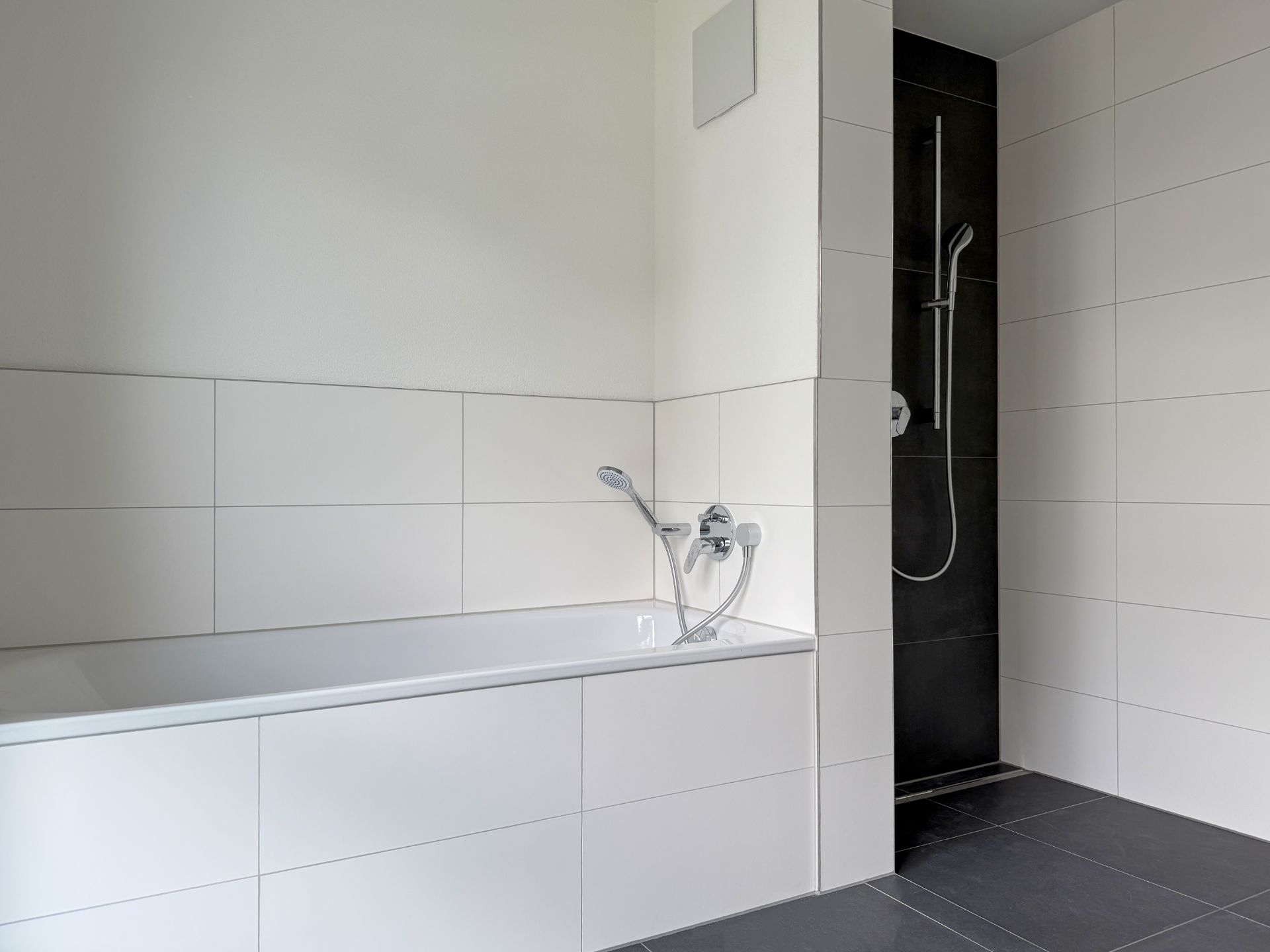 Modernes Bad mit weißer Badewanne und separater Dusche mit schwarzer Wand.