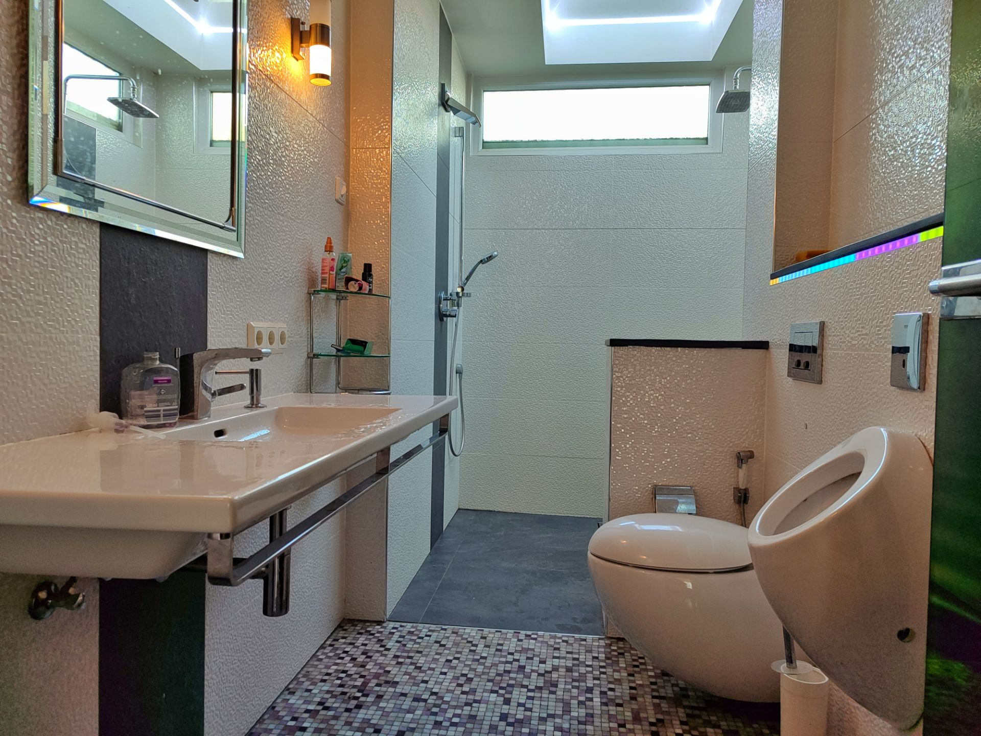 Modernes Badezimmer mit Waschbecken, Toilette, Urinal und bodengleicher Dusche.