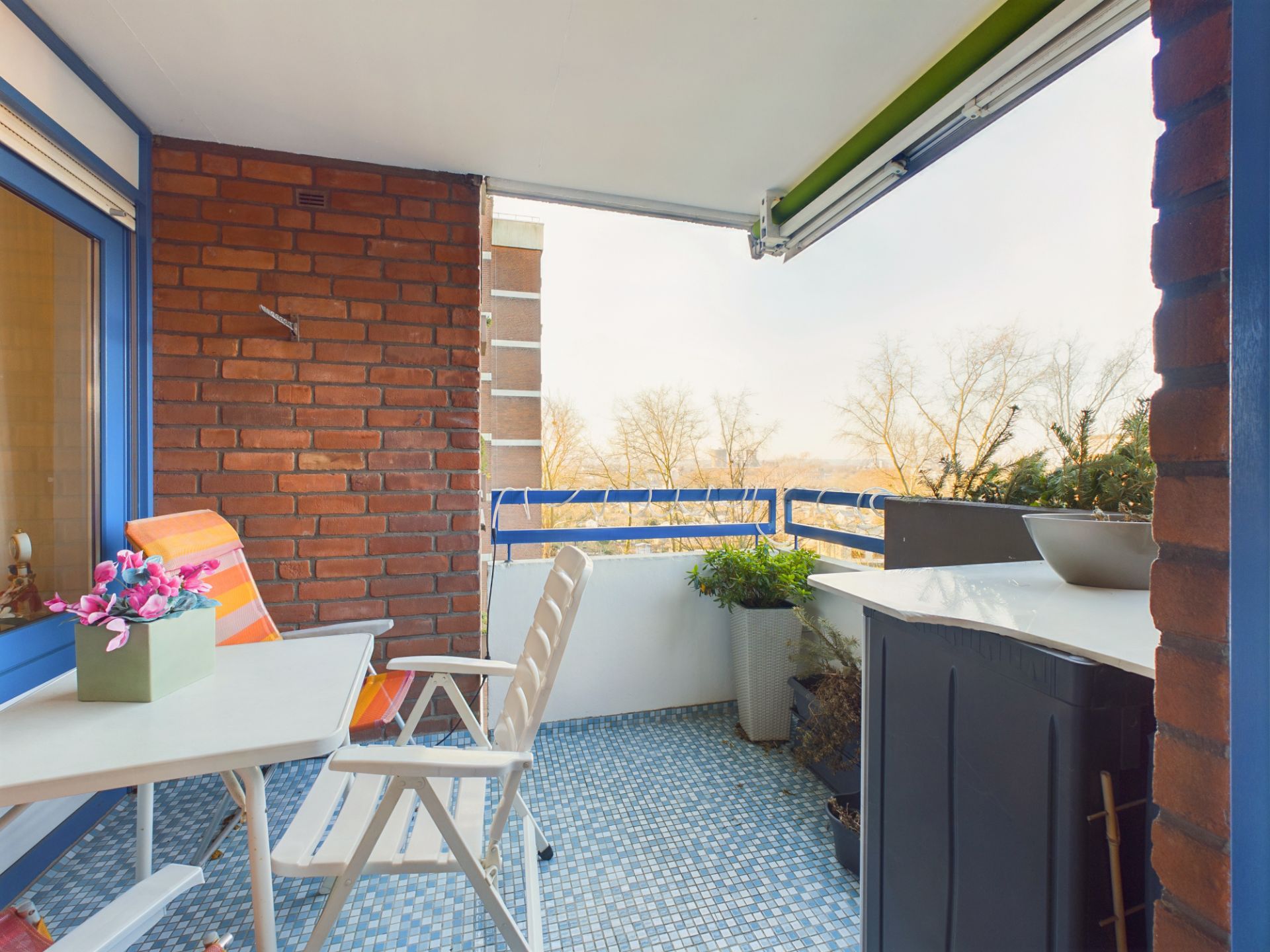 Balkon mit Tisch, Stühlen, Blumendeko und Pflanzen, Boden mit blauen Fliesen.