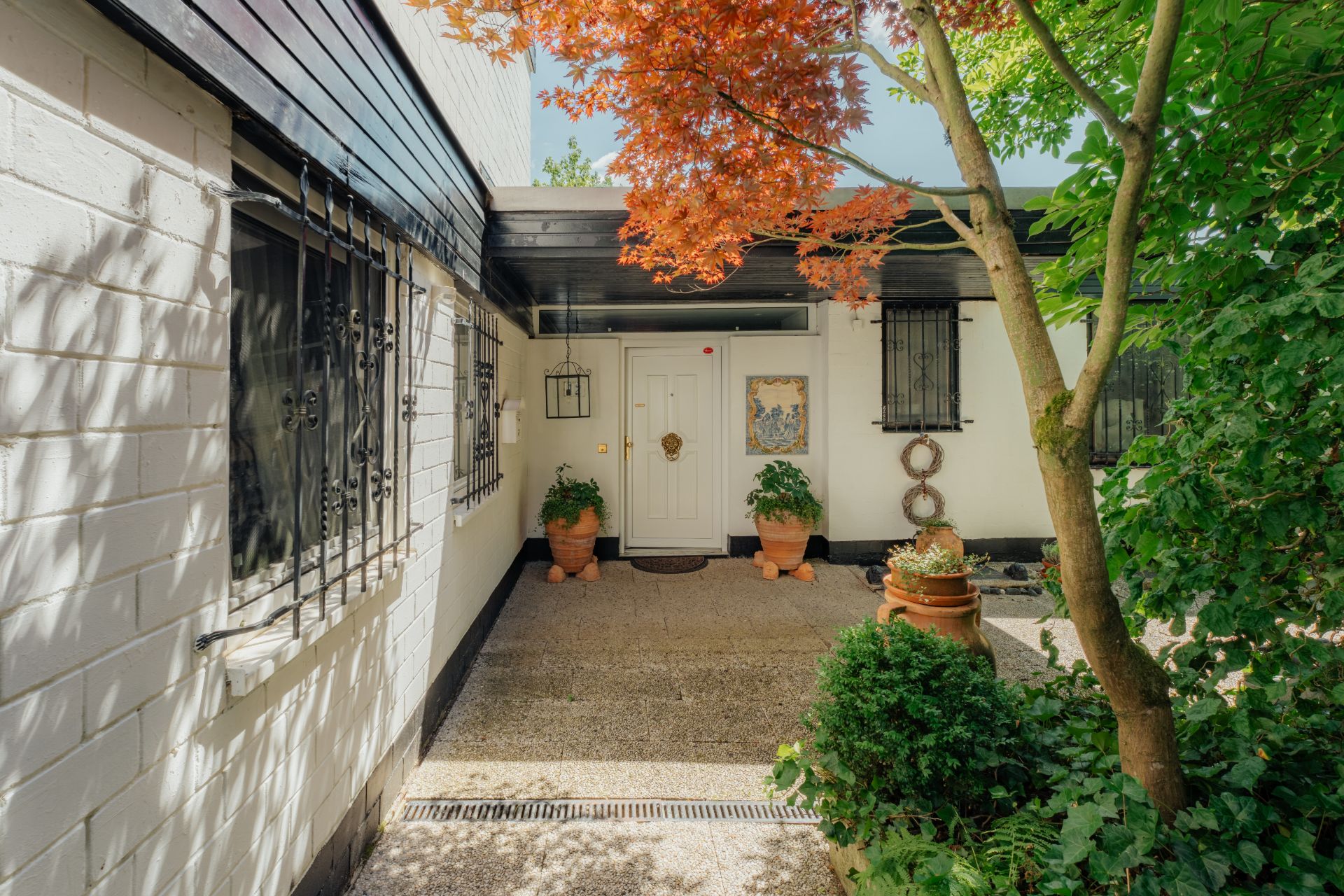 Eingangsbereich eines Hauses mit weißen Wänden, Pflanzen und Bäumen im Vordergrund.