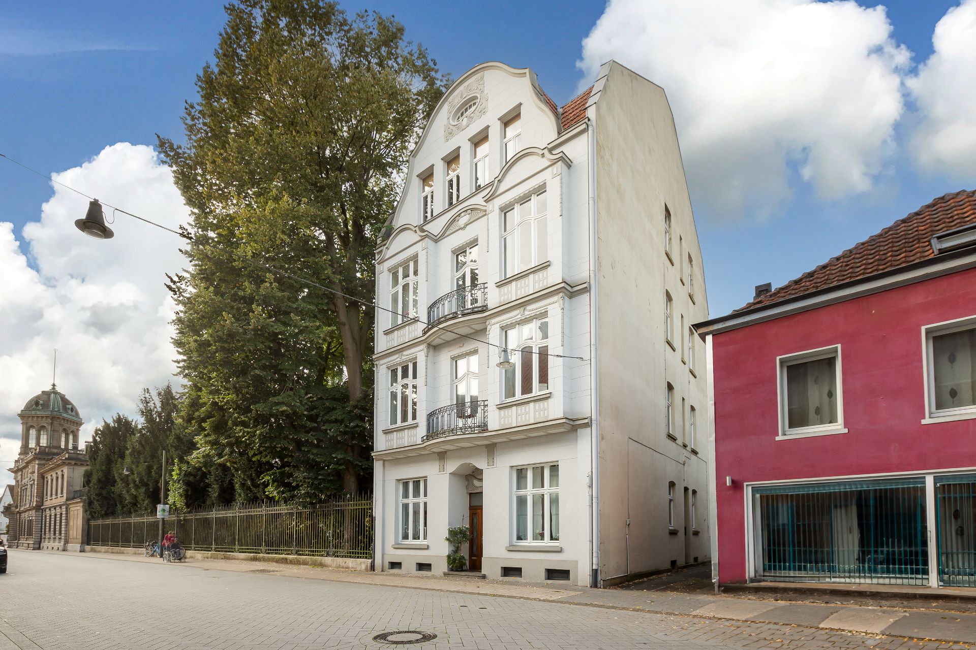 Mehrstöckiges Wohnhaus mit Balkonen und weißer Fassade an einer ruhigen Straße.