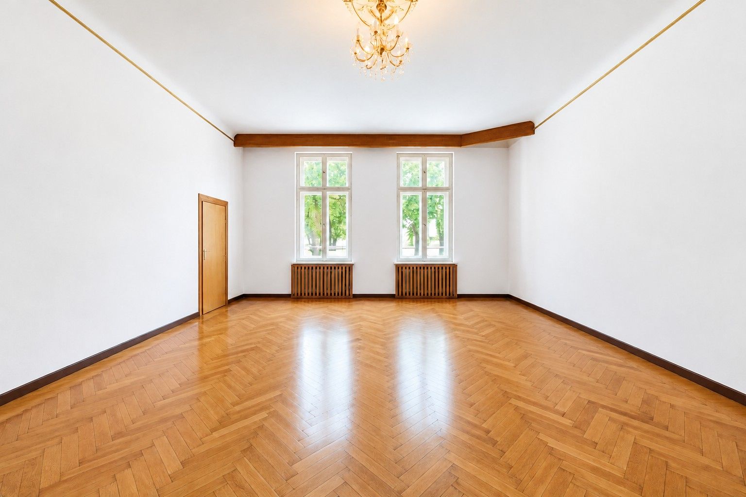 Leerer Raum mit Holzboden, weißen Wänden, zwei Fenstern und Kronleuchter.