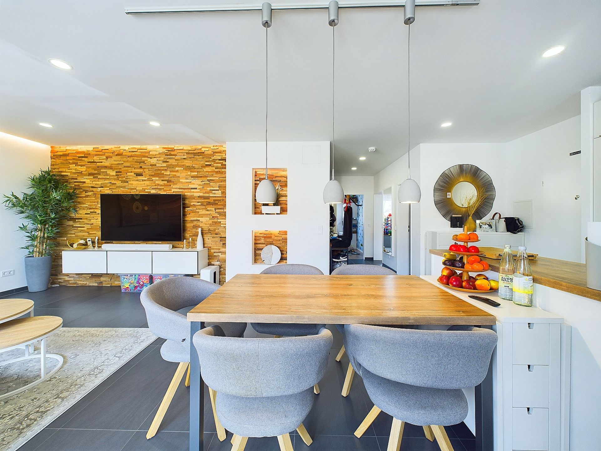 Modernes Wohn- und Esszimmer mit Holztisch, grauen Stühlen und offener Küche.