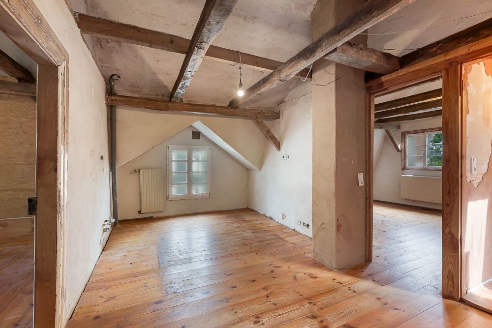 Leerer Dachbodenraum mit Holzboden, sichtbaren Balken und Fenstern.