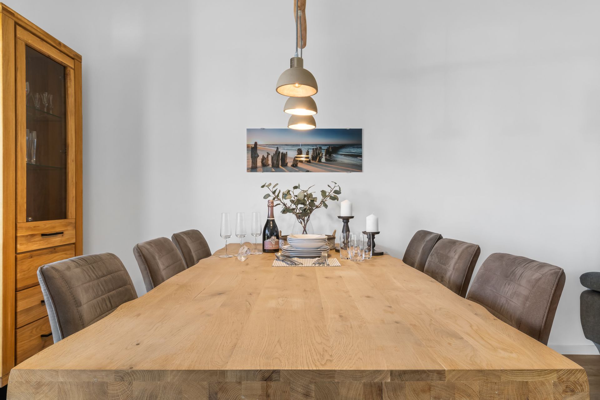 Esszimmer mit großem Holztisch, sechs Stühlen, Wandbild und drei Hängelampen.