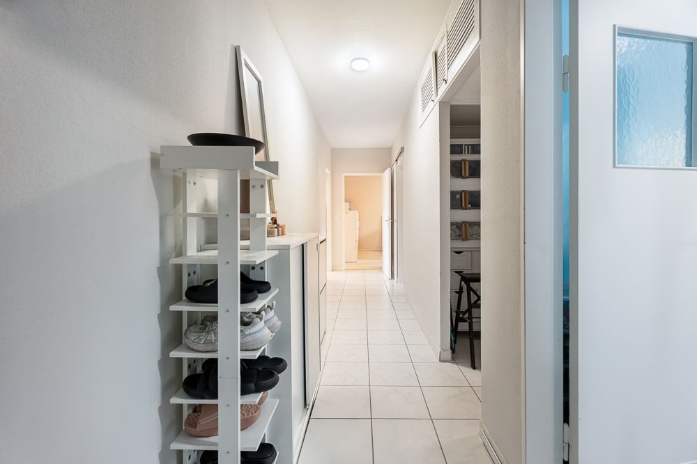 Heller Flur mit weißem Fliesenboden, Schuhregal und Zugang zu mehreren Zimmern.