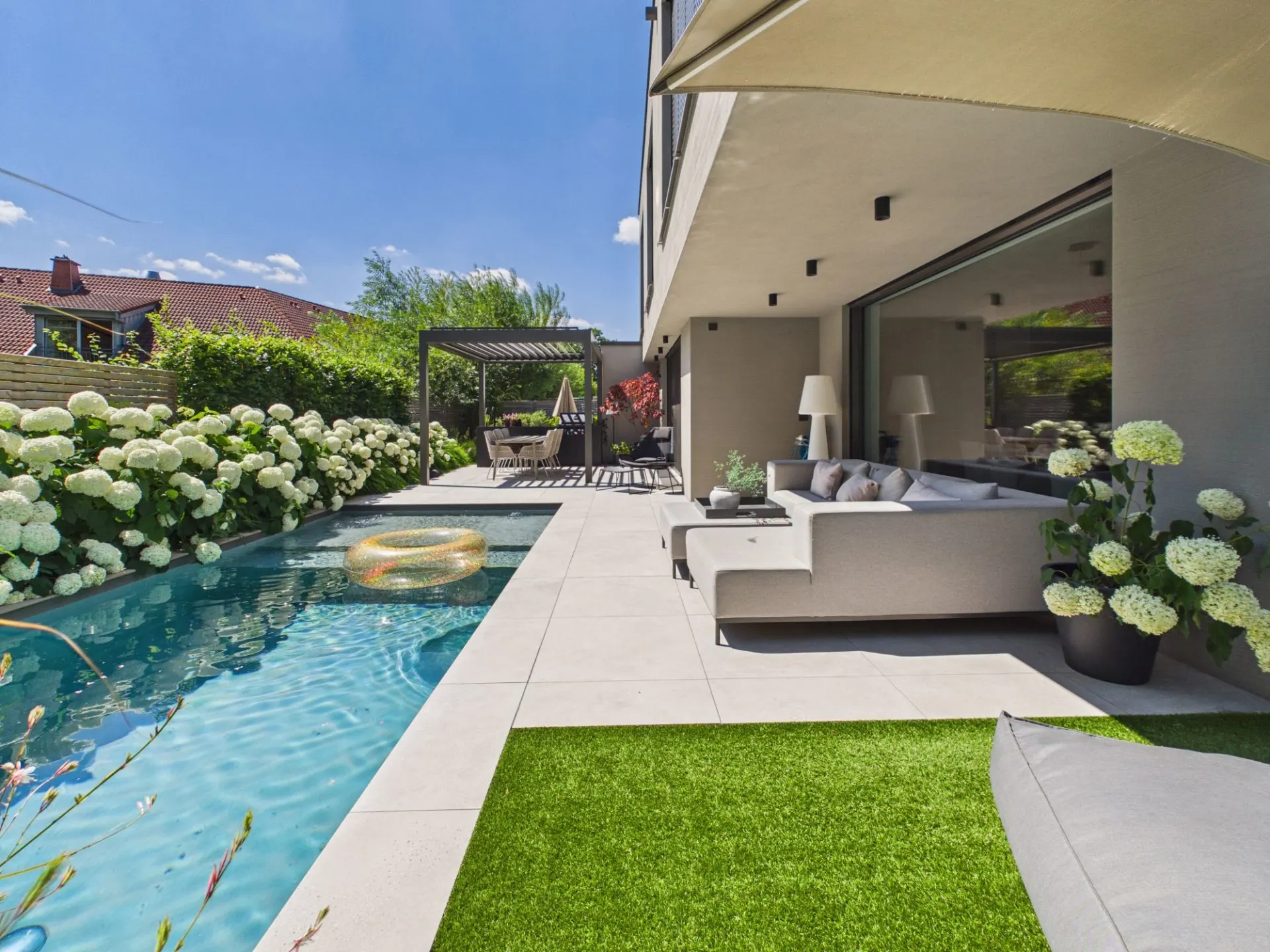 Moderne Terrasse mit Sofa, Pool und Blumen im Garten eines Wohnhauses bei Sonnenschein.