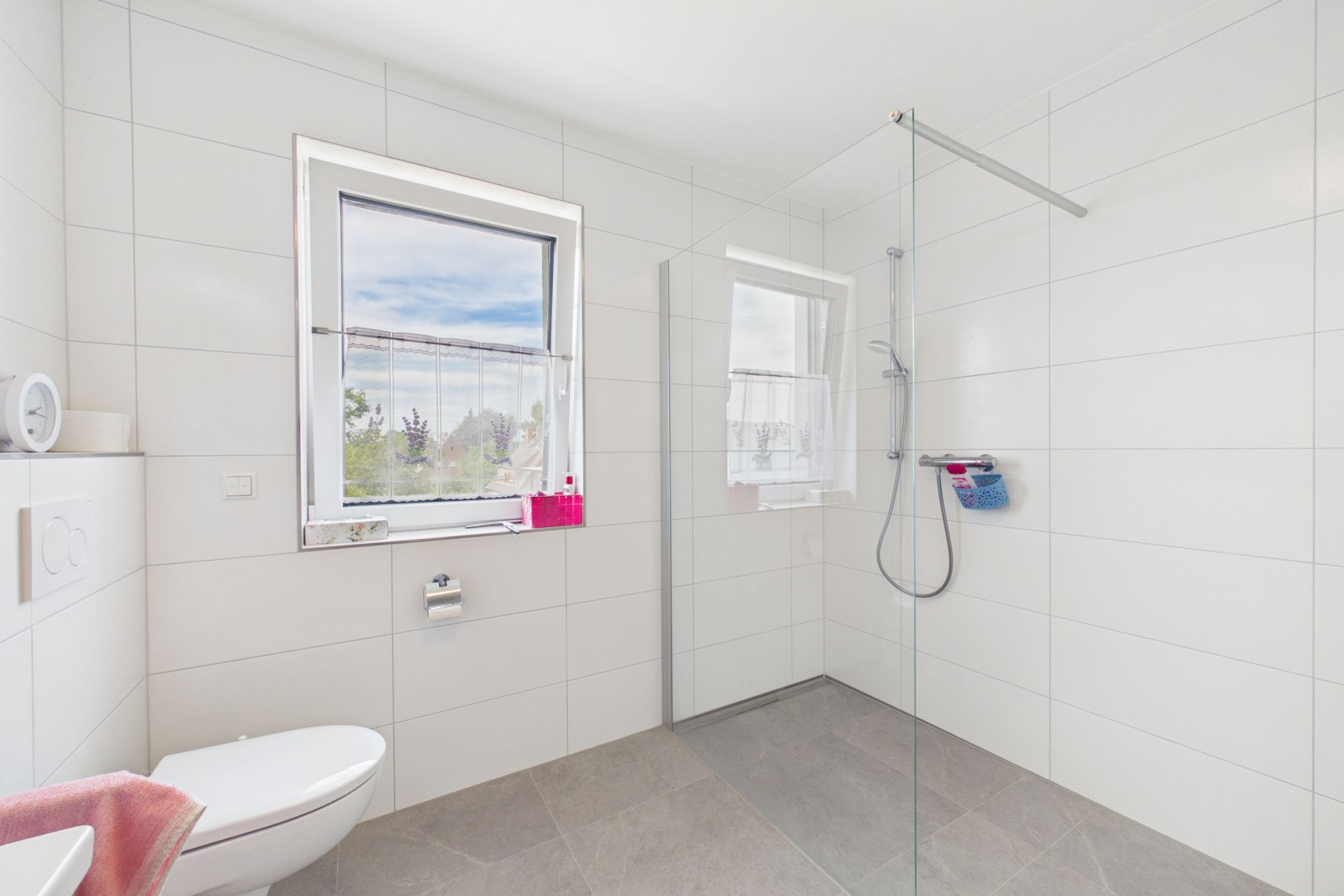 Modernes, helles Bad mit ebenerdiger Dusche, WC und Fenster.