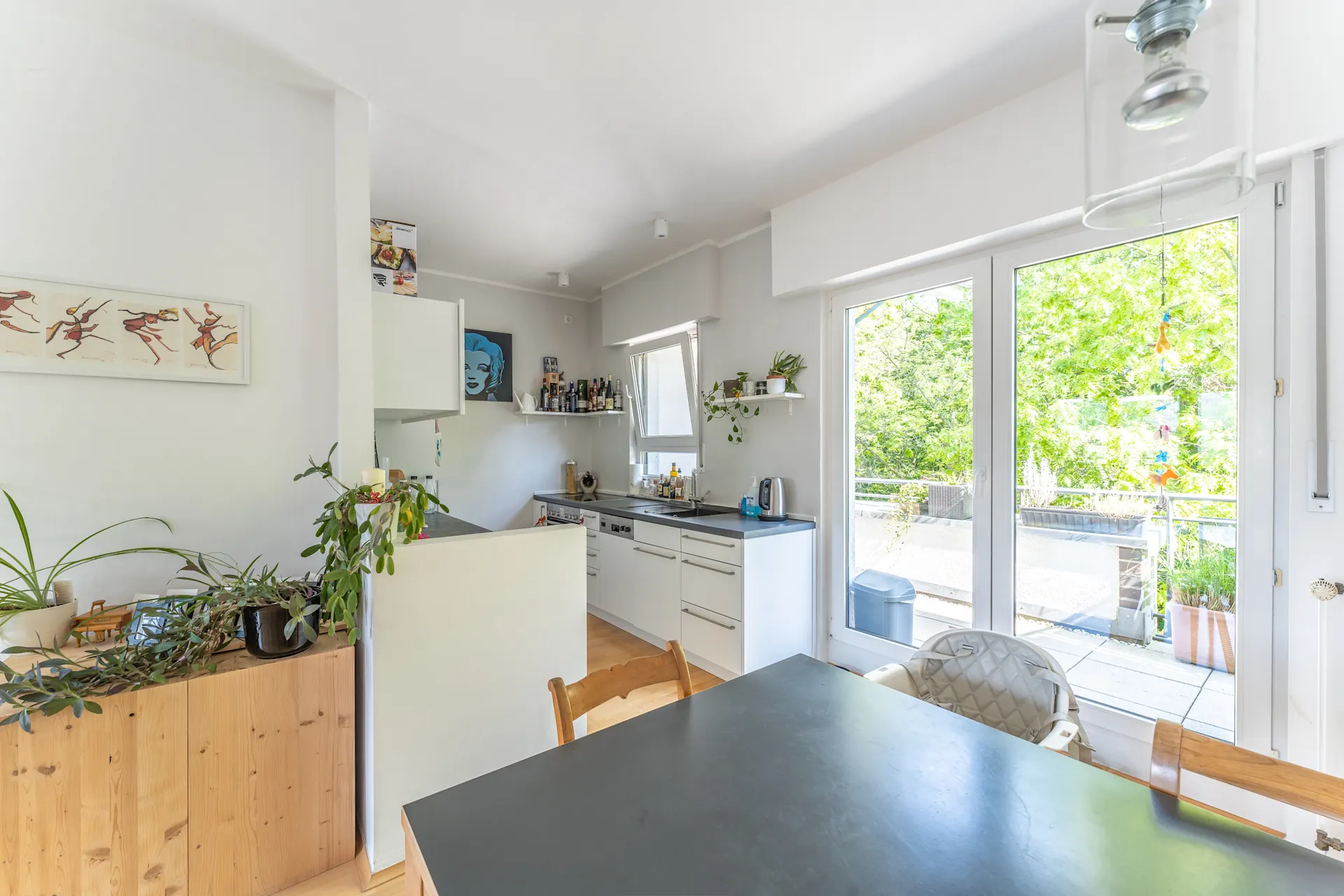 Helle Küche mit Esstisch, Pflanzen und Zugang zu einer Terrasse mit viel Grün draußen.