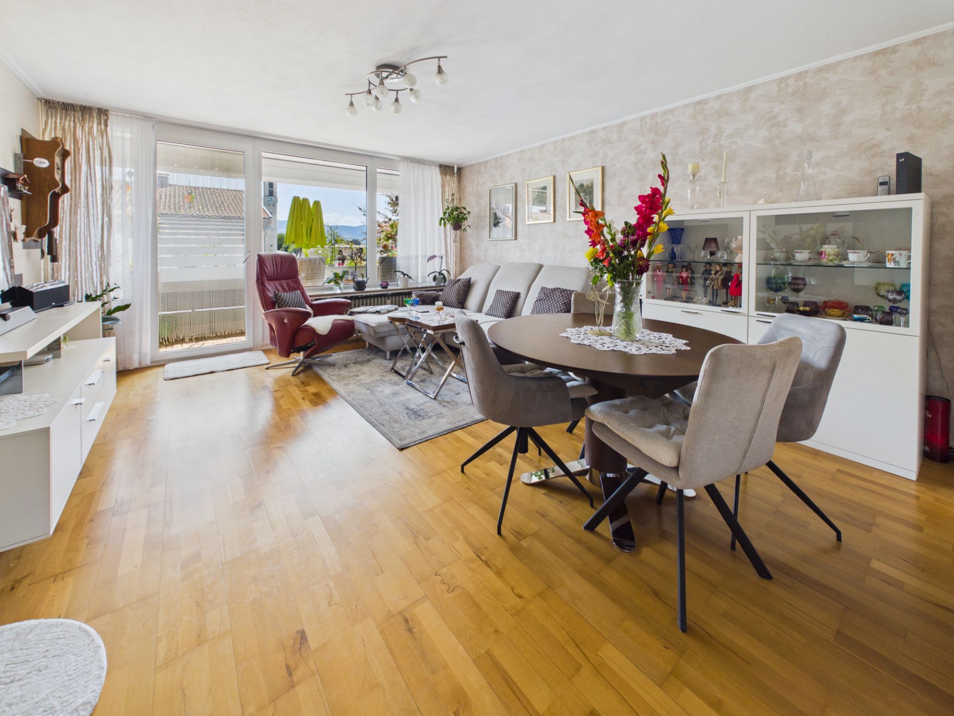 Helles Wohnzimmer mit Essbereich, Sofa, Sessel, großem Fenster und Holzboden.