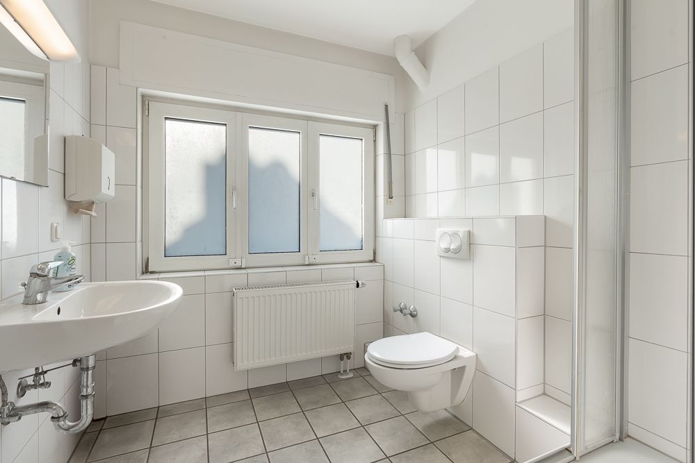 Helles Badezimmer mit Waschbecken, WC, Fenster und gefliestem Boden.