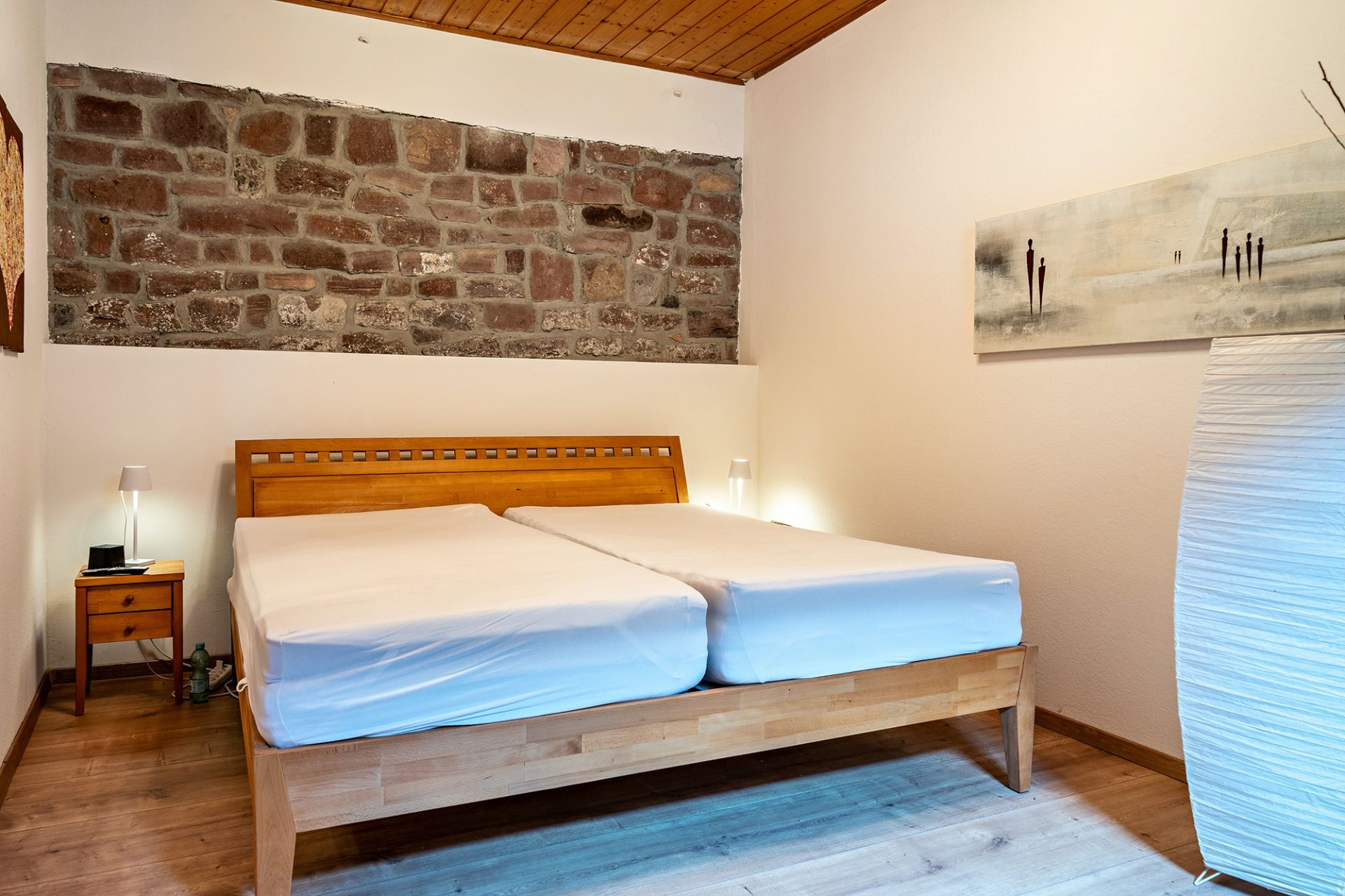 Schlafzimmer mit zwei Einzelbetten, Holzboden und sichtbarer Steinwand.