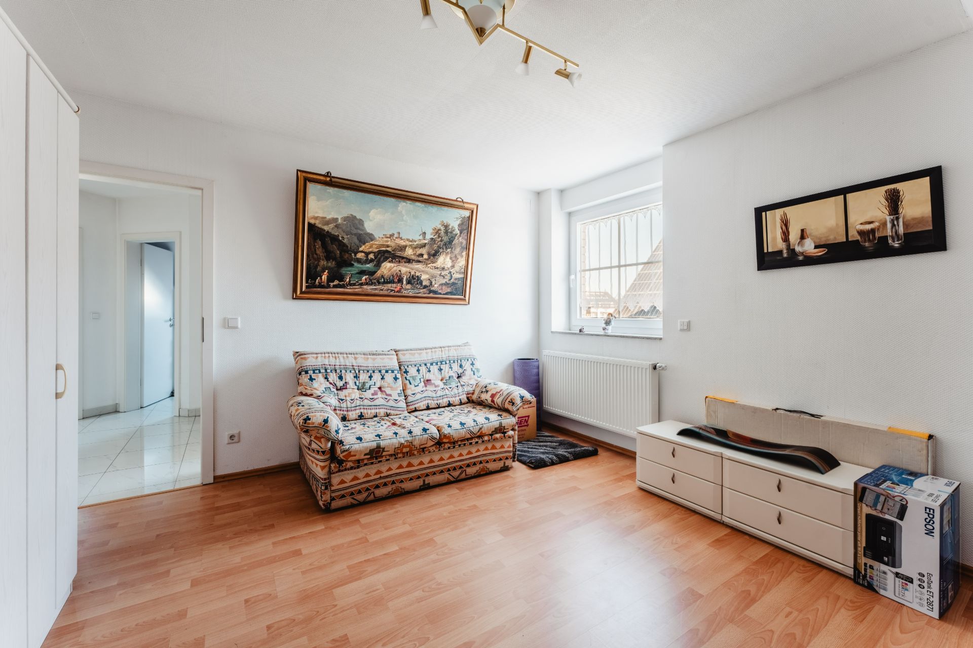 Helles Wohnzimmer mit gemustertem Sofa, Holzboden, Kunstwerken und einem Fenster.