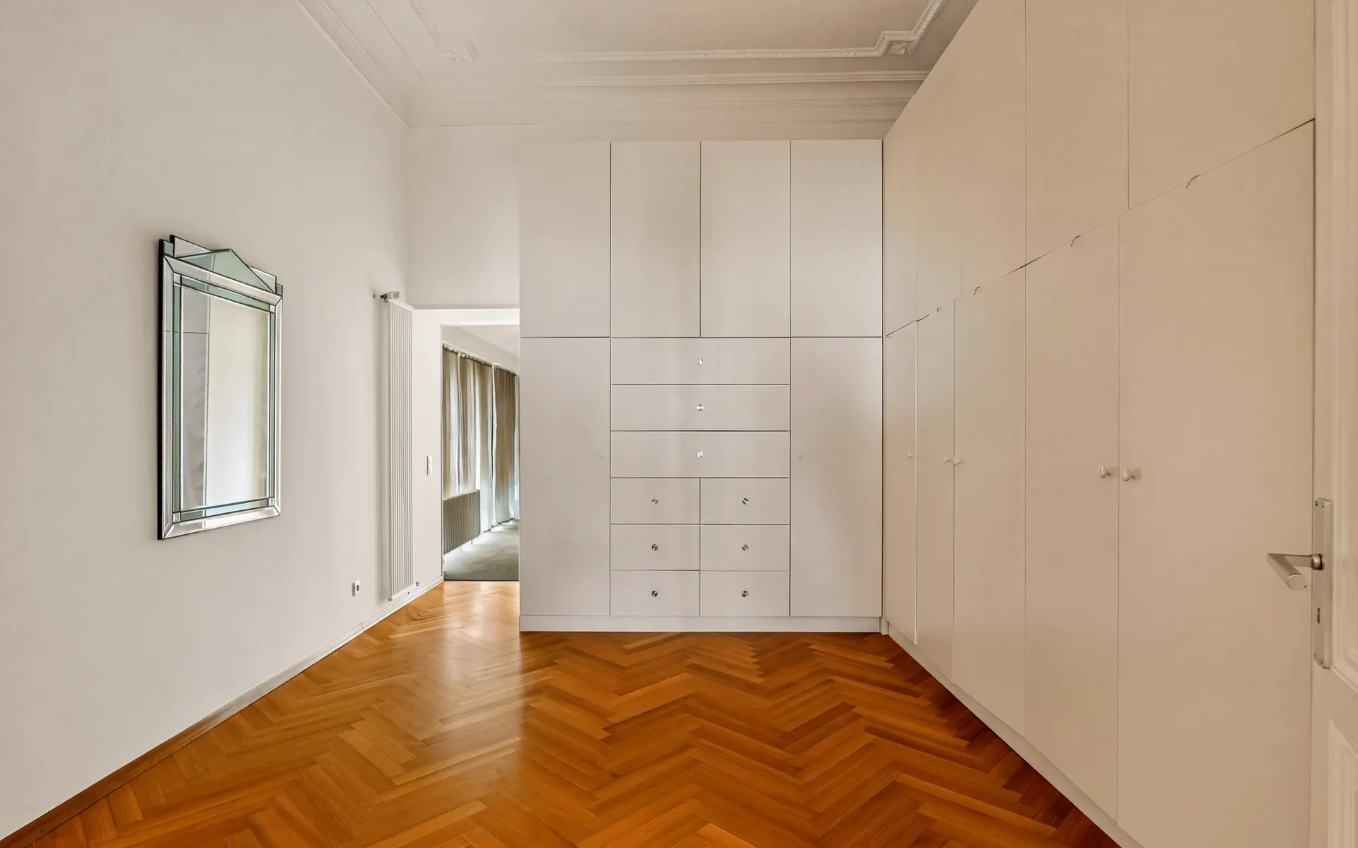 Heller Raum mit Parkettboden, großem weißen Einbauschrank und Spiegel an der Wand.