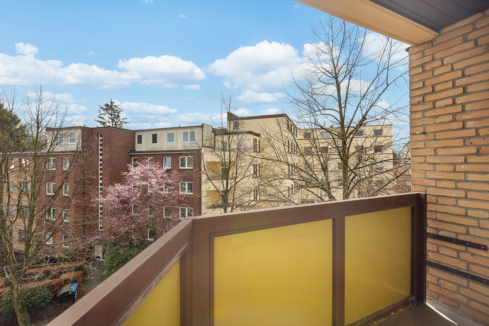 Blick von einem Balkon mit gelbem Geländer auf Wohngebäude und blühenden Baum.