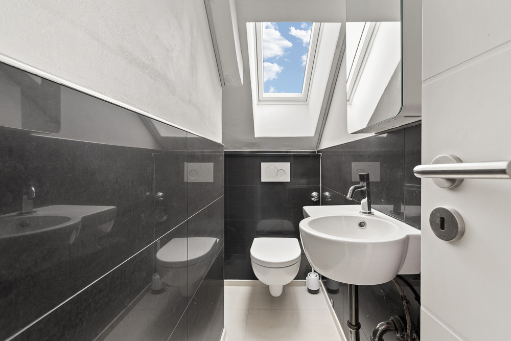 Modernes Gäste-WC mit Wandtoilette, Waschbecken und Dachfenster unter einer Schräge.