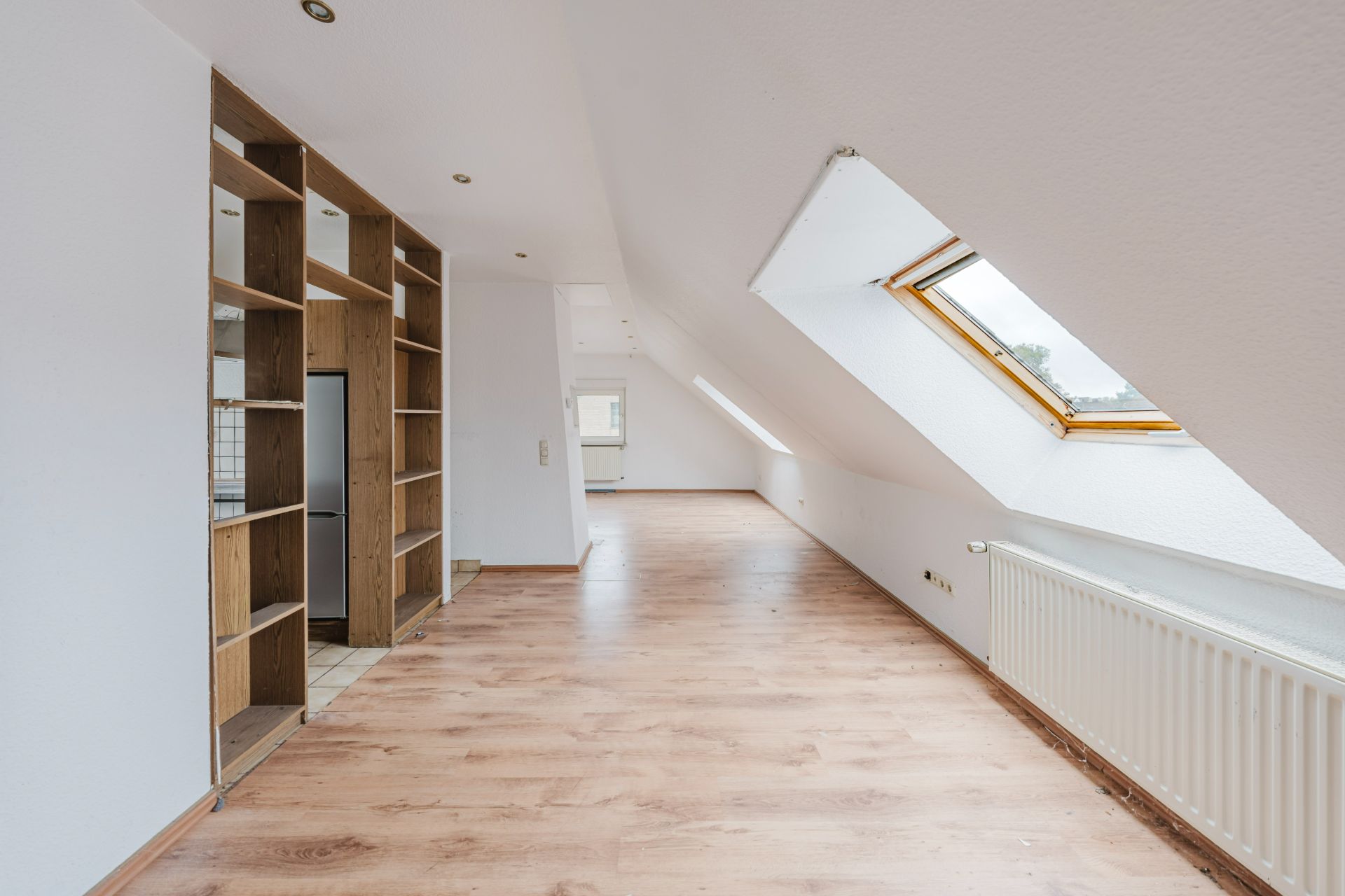 Heller Dachgeschossraum mit Holzfußboden, Regalen und großen Dachfenstern.
