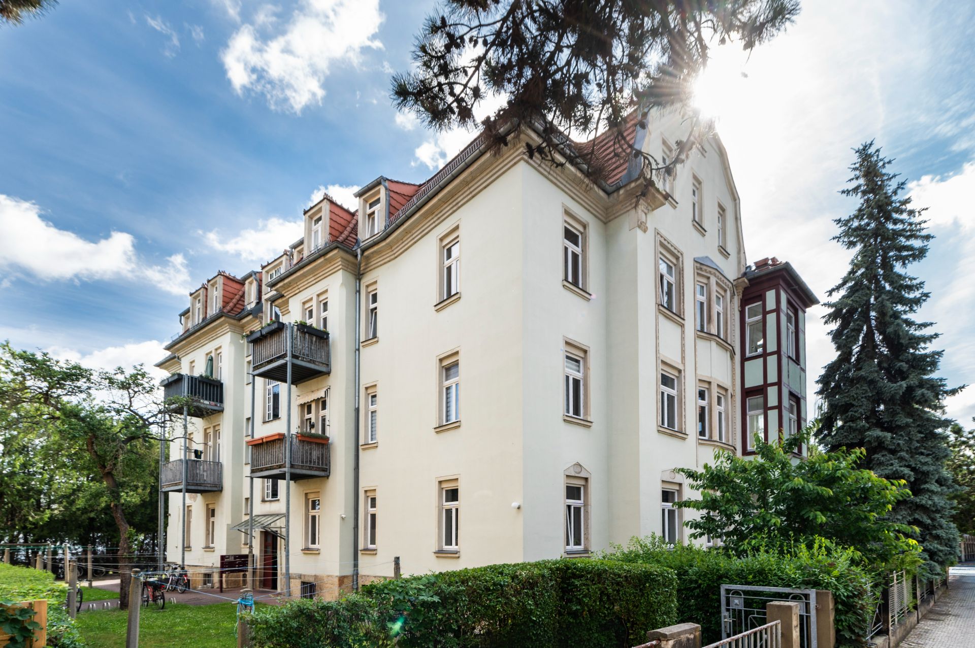 Mehrstöckiges Wohngebäude mit Balkonen und Garten, umgeben von Bäumen.