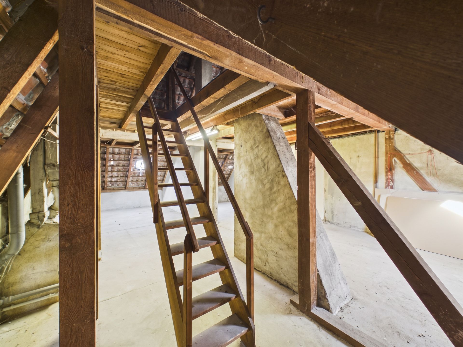 Unrenovierter Dachboden mit Holzbalken und einer Holztreppe zur oberen Etage.