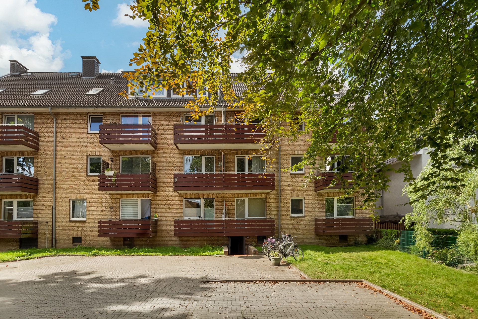Dreistöckiges Wohnhaus mit Balkonen, Backsteinfassade, Vorgarten und Fahrrädern vor dem Eingang.