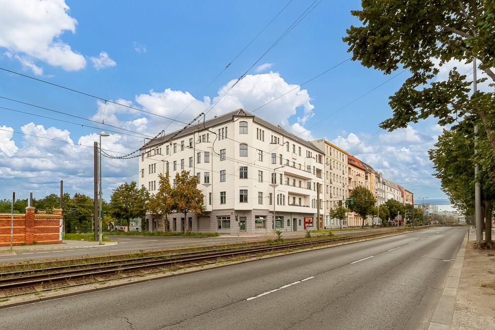 Mehrstöckiges Wohngebäude an einer Straße mit Straßenbahnschienen und Bäumen.