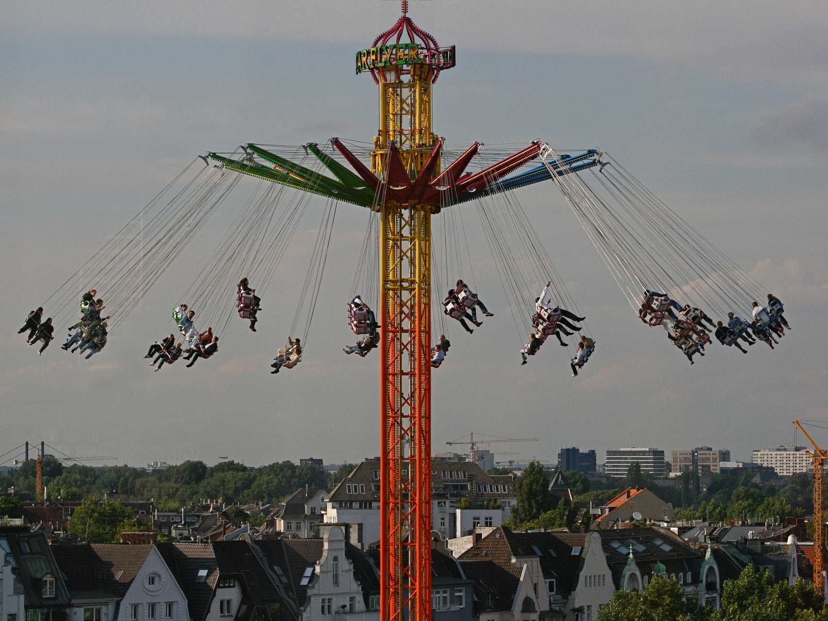 Kettenkarussell mit vielen Menschen, im Hintergrund Wohnhäuser und Bäume.