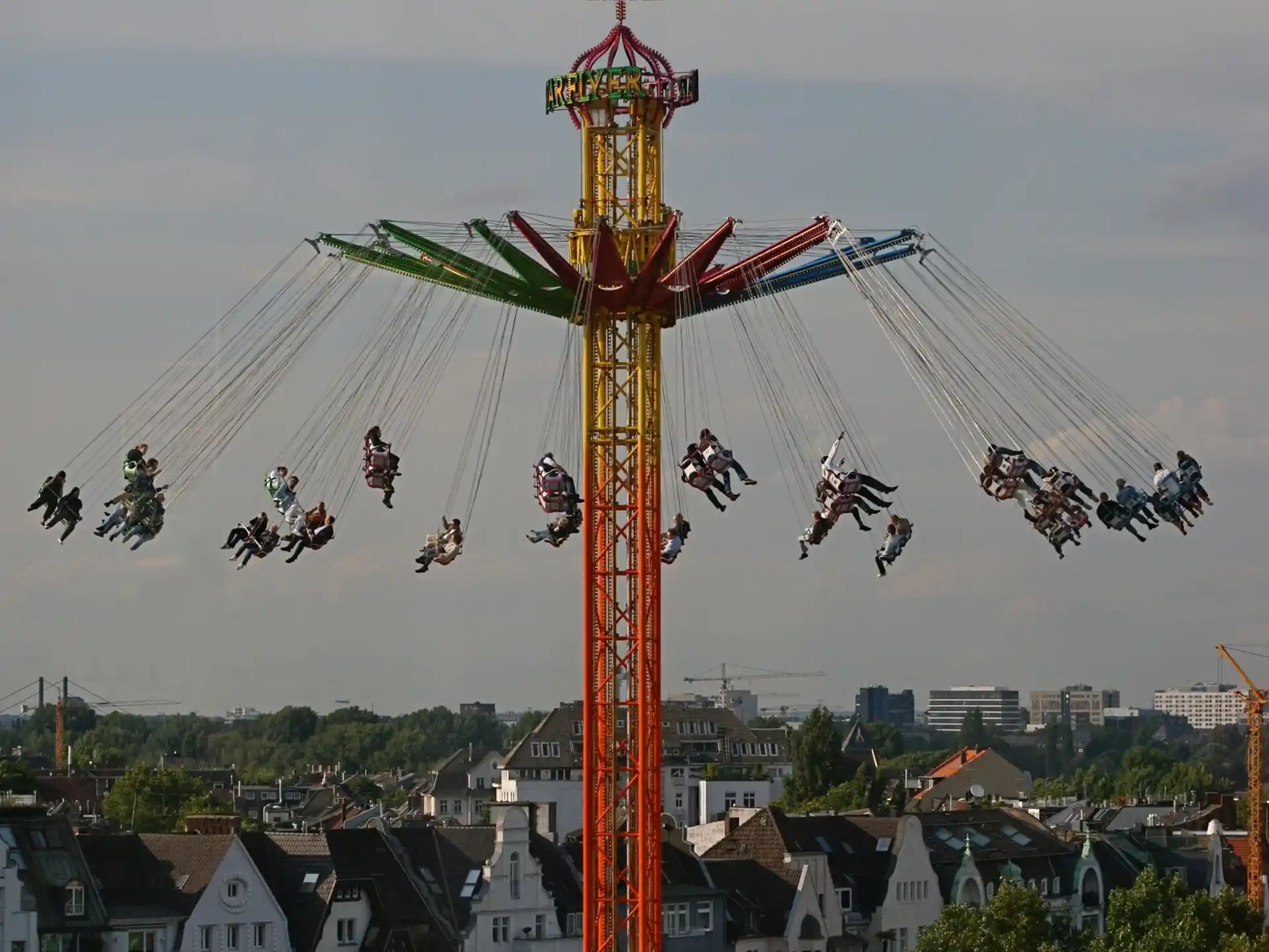 Kettenkarussell mit vielen Menschen, im Hintergrund Wohnhäuser und Bäume.