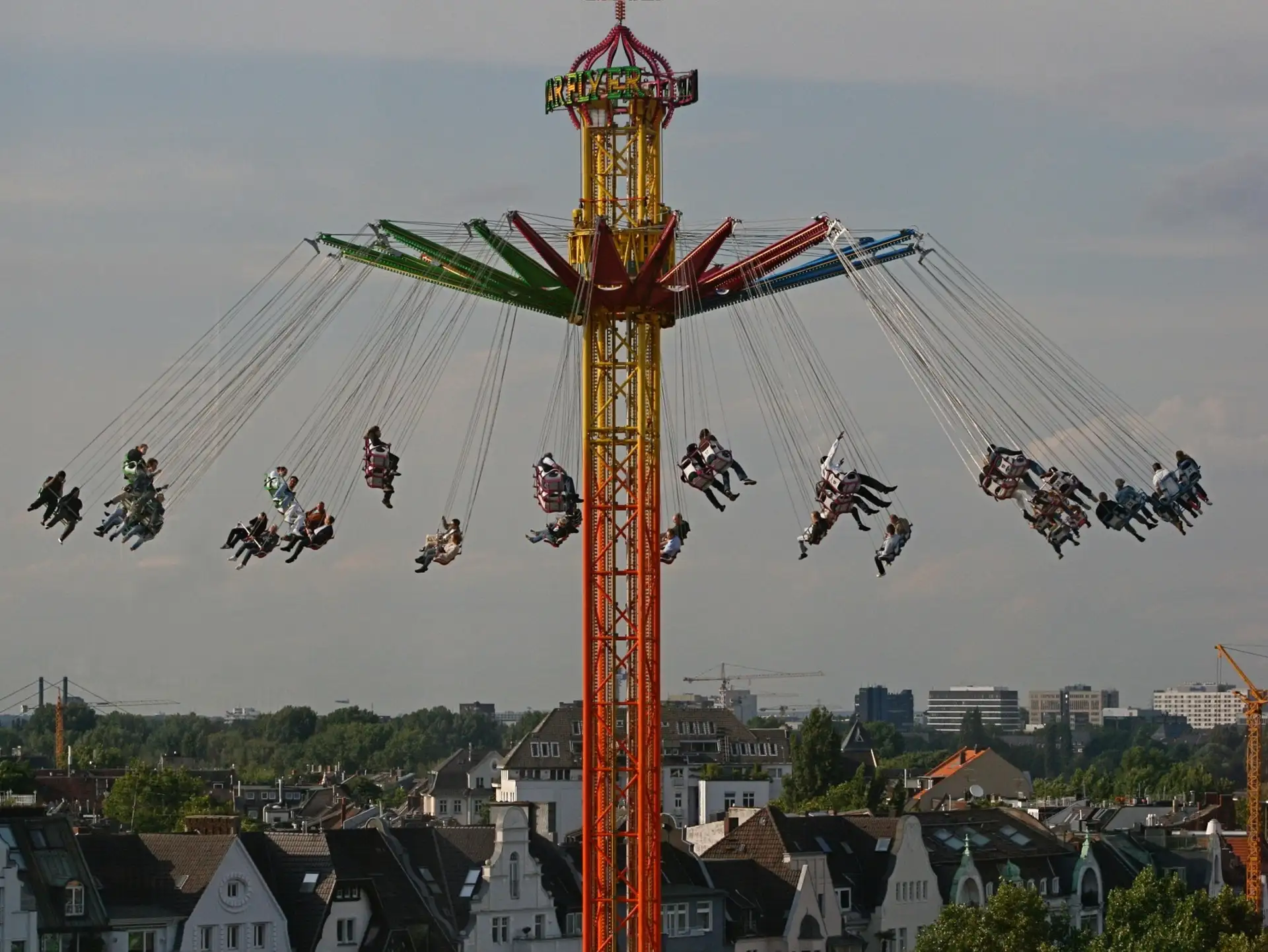 Kettenkarussell mit vielen Menschen, im Hintergrund Wohnhäuser und Bäume.