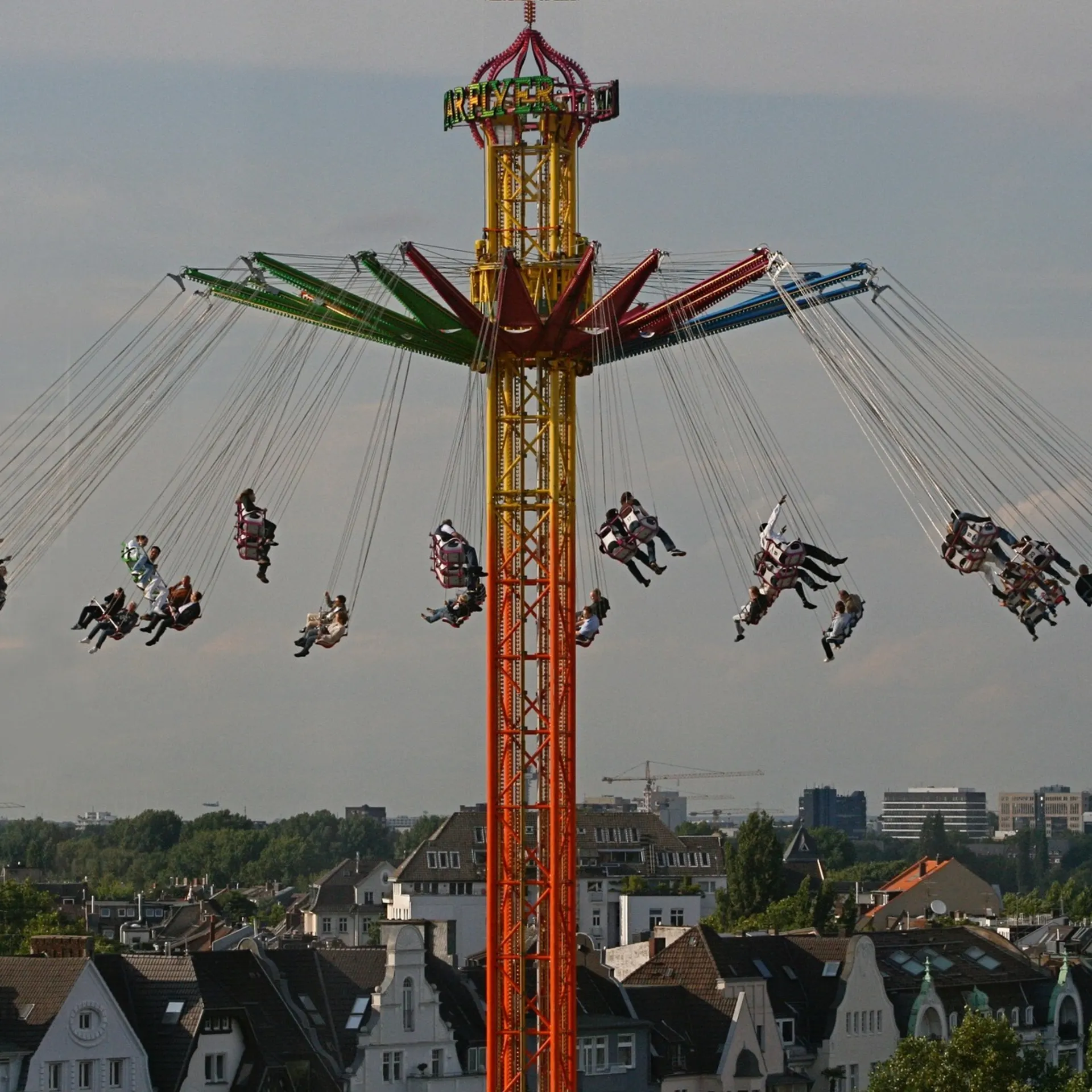 Kettenkarussell mit vielen Menschen, im Hintergrund Wohnhäuser und Bäume.