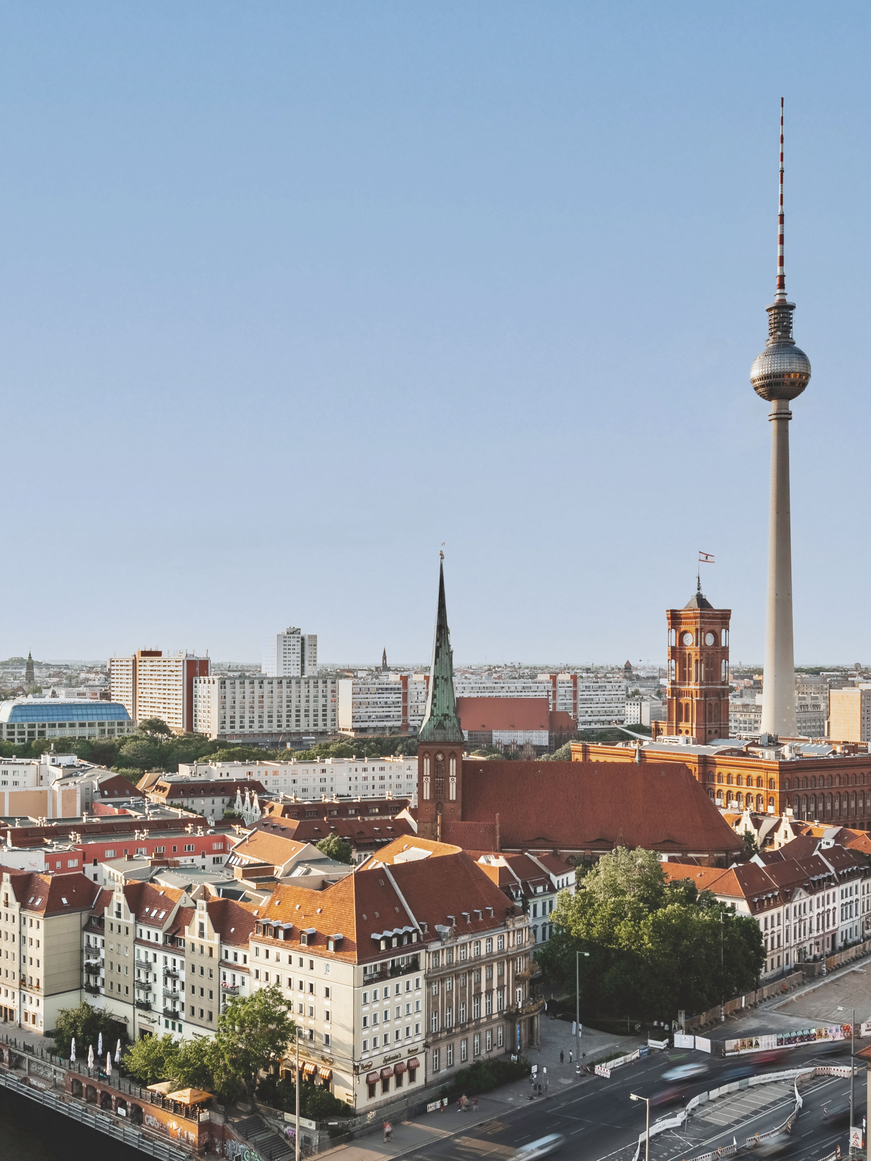 Stadtansicht mit roten Dächern, Kirche, Fernsehturm und blauem Himmel.