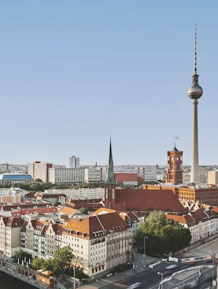 Stadtansicht mit roten Dächern, Kirche, Fernsehturm und blauem Himmel.