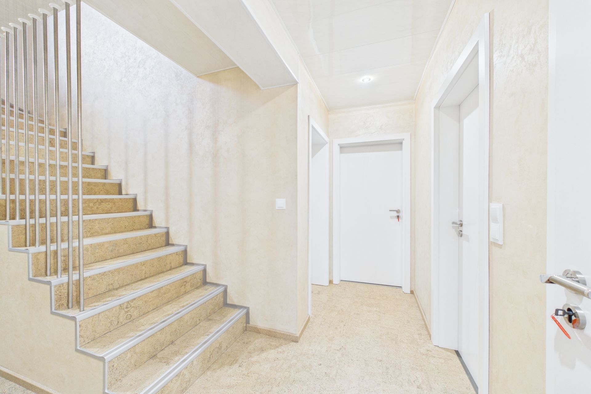 Heller Flur mit Treppe und mehreren weißen Türen in einem Wohnhaus.