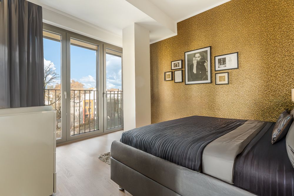 Schlafzimmer mit großem Bett, goldener Wand, Bildern und bodentiefen Fenstern mit Blick ins Freie.