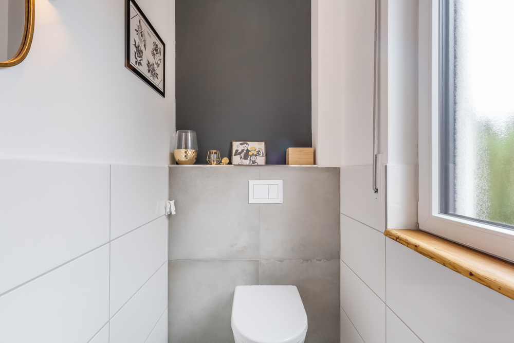 Modernes, helles Badezimmer mit WC, Fenster und Dekoration auf einem Ablagebrett.