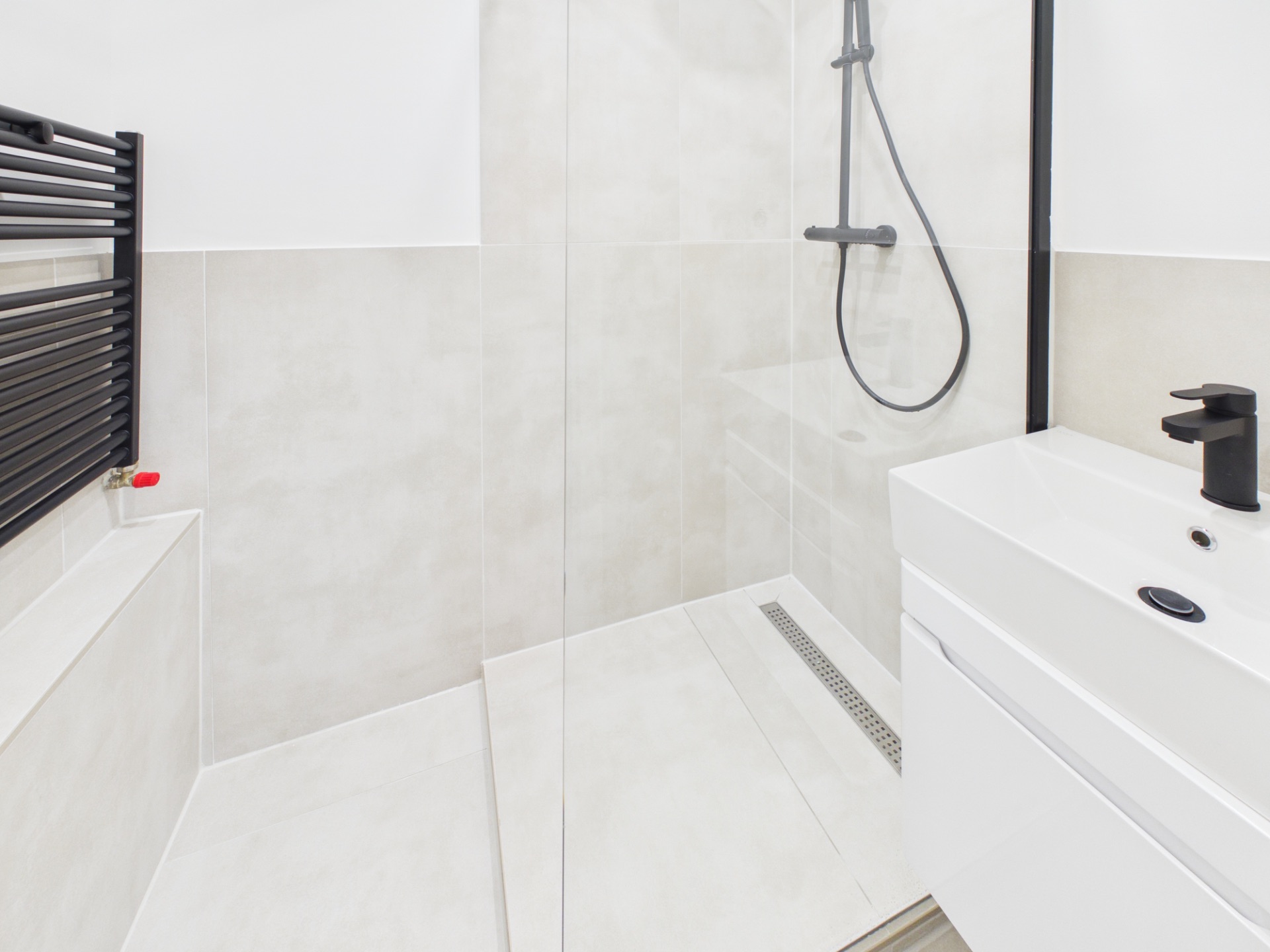 Modernes Badezimmer mit begehbarer Dusche, schwarzer Armatur und weißem Waschbecken.