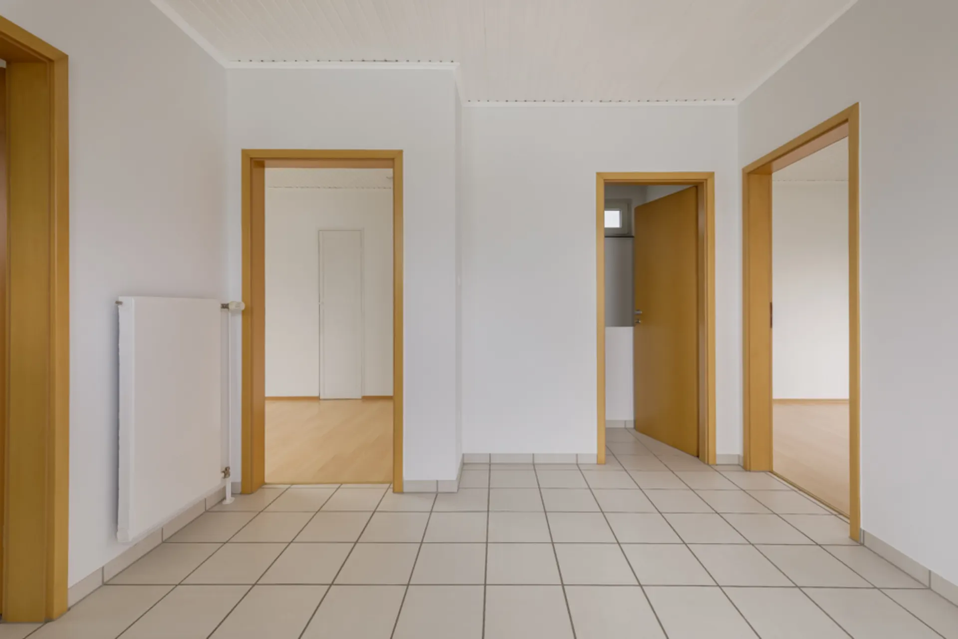 Leerer Flur mit weißen Wänden, Fliesenboden und drei offenen Türen zu angrenzenden Zimmern.
