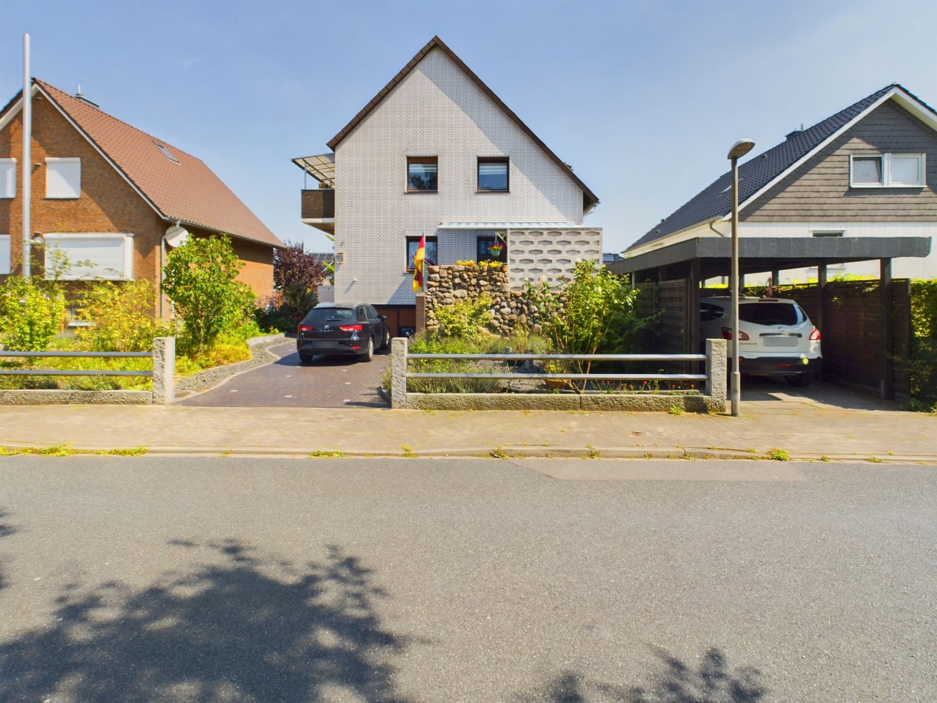Zwei Einfamilienhäuser mit Einfahrten und geparkten Autos, vorne Straße und Vorgarten.