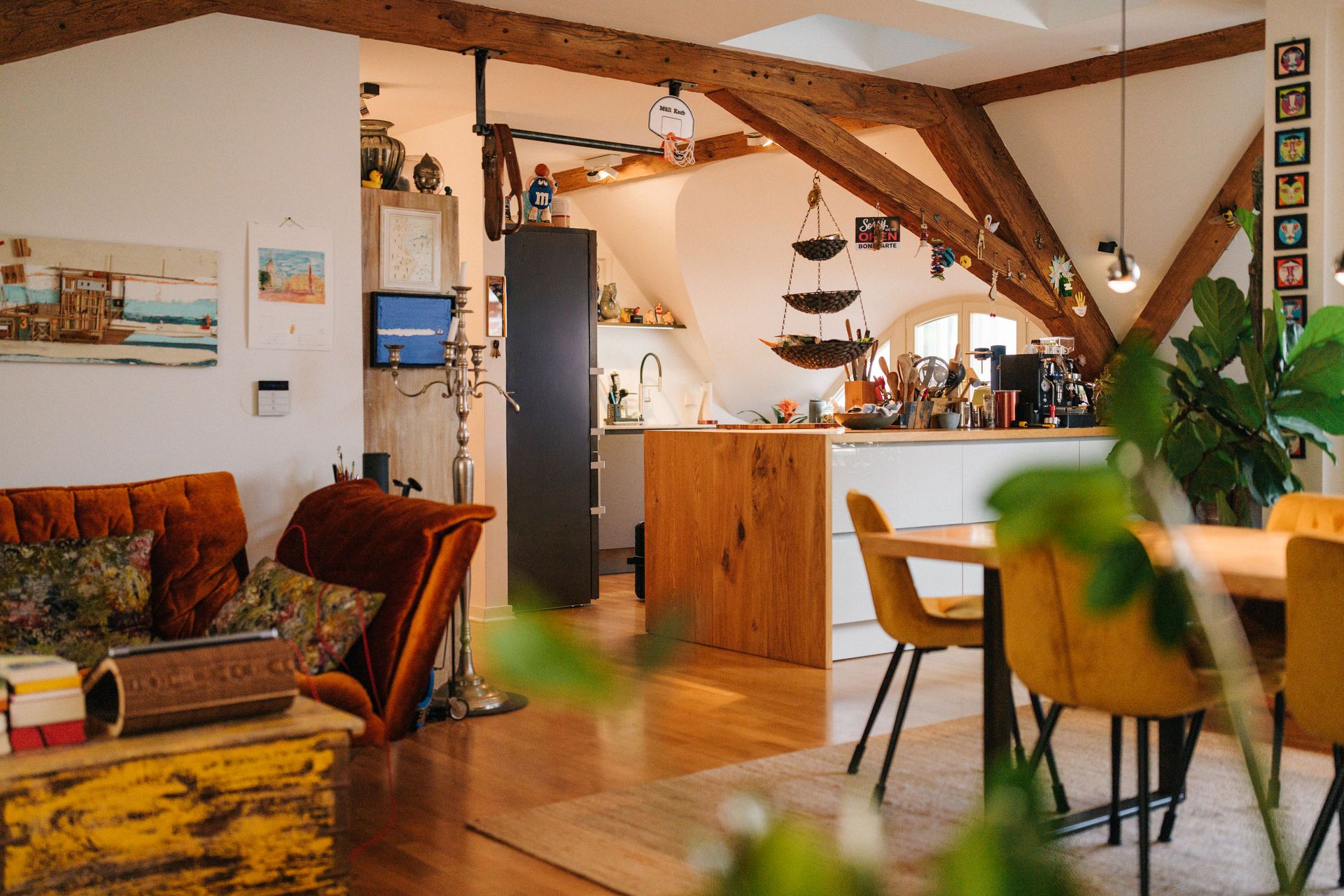 Gemütliches Wohnzimmer mit Holzbalken, offener Küche, Esstisch und Pflanzen.